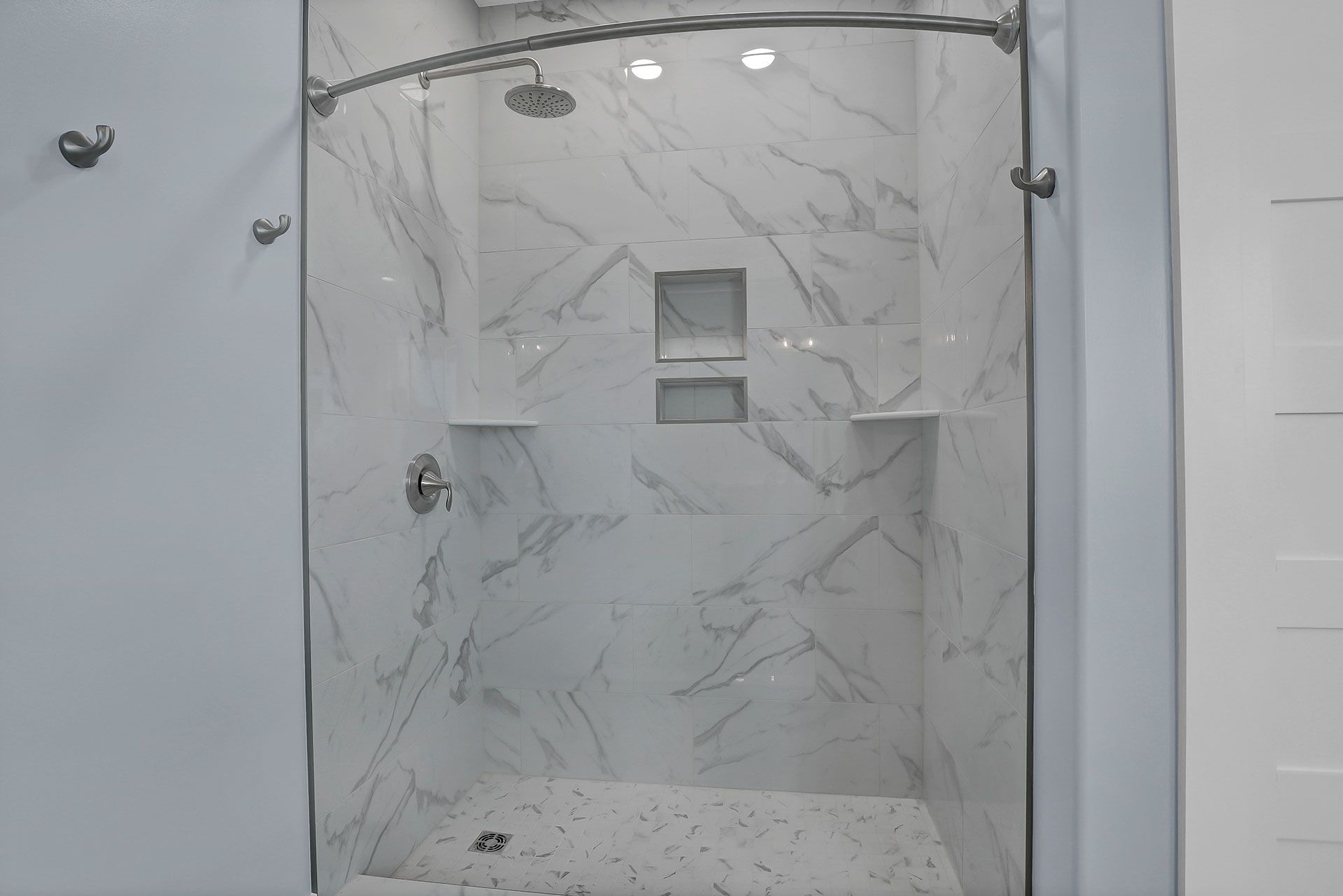 Modern shower with white marble-look tile, glass doors, and built-in shelves.