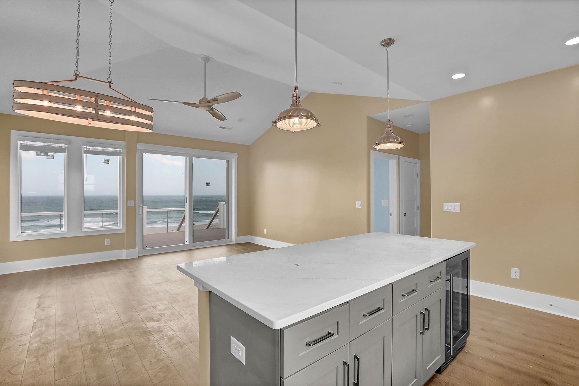 Open-concept kitchen with ocean view, gray island, wood floor, pendant lights, and sliding glass doors.