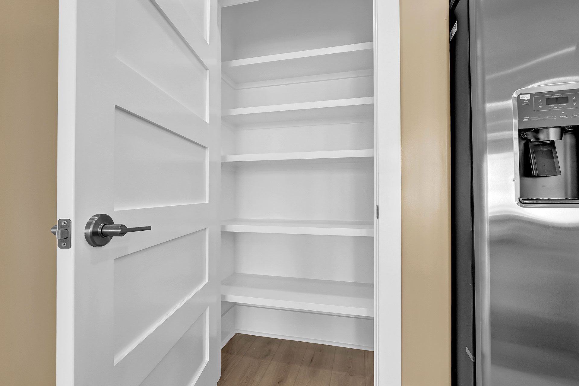 White pantry with shelves next to a refrigerator. Door is open.