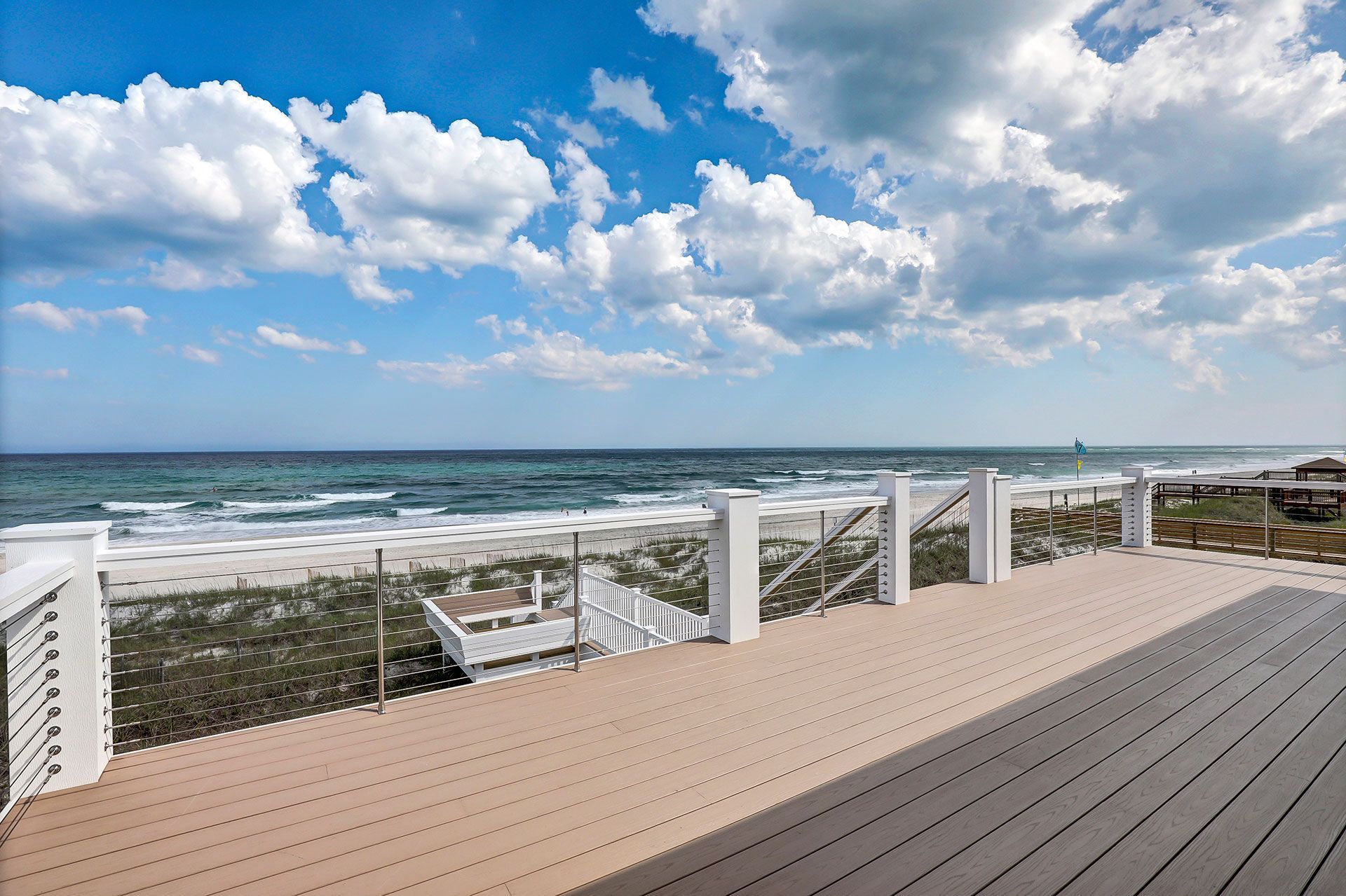 Deck overlooking ocean and beach under a partly cloudy blue sky.