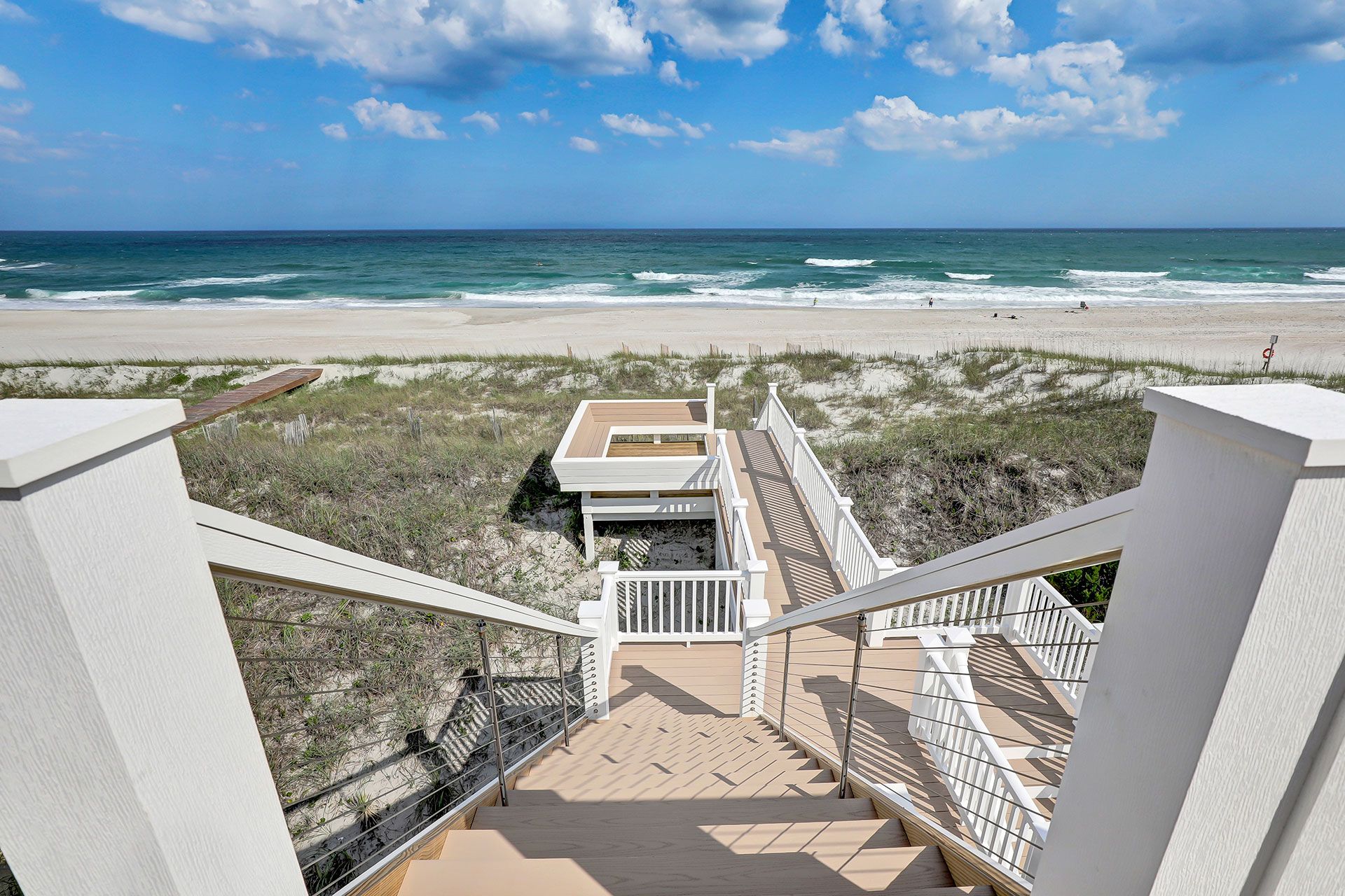 Staircase leads to a beach with white sand and blue ocean under a bright sky.