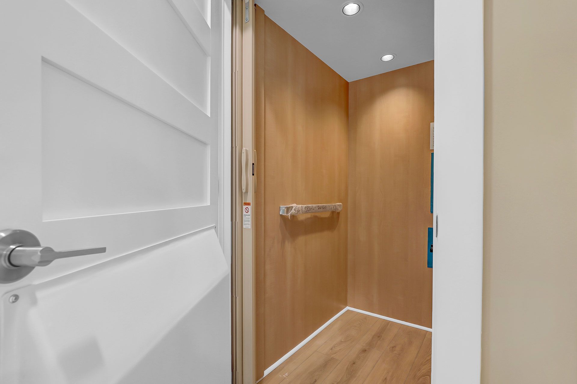 White door open to reveal a wooden-paneled elevator, with a grab bar.
