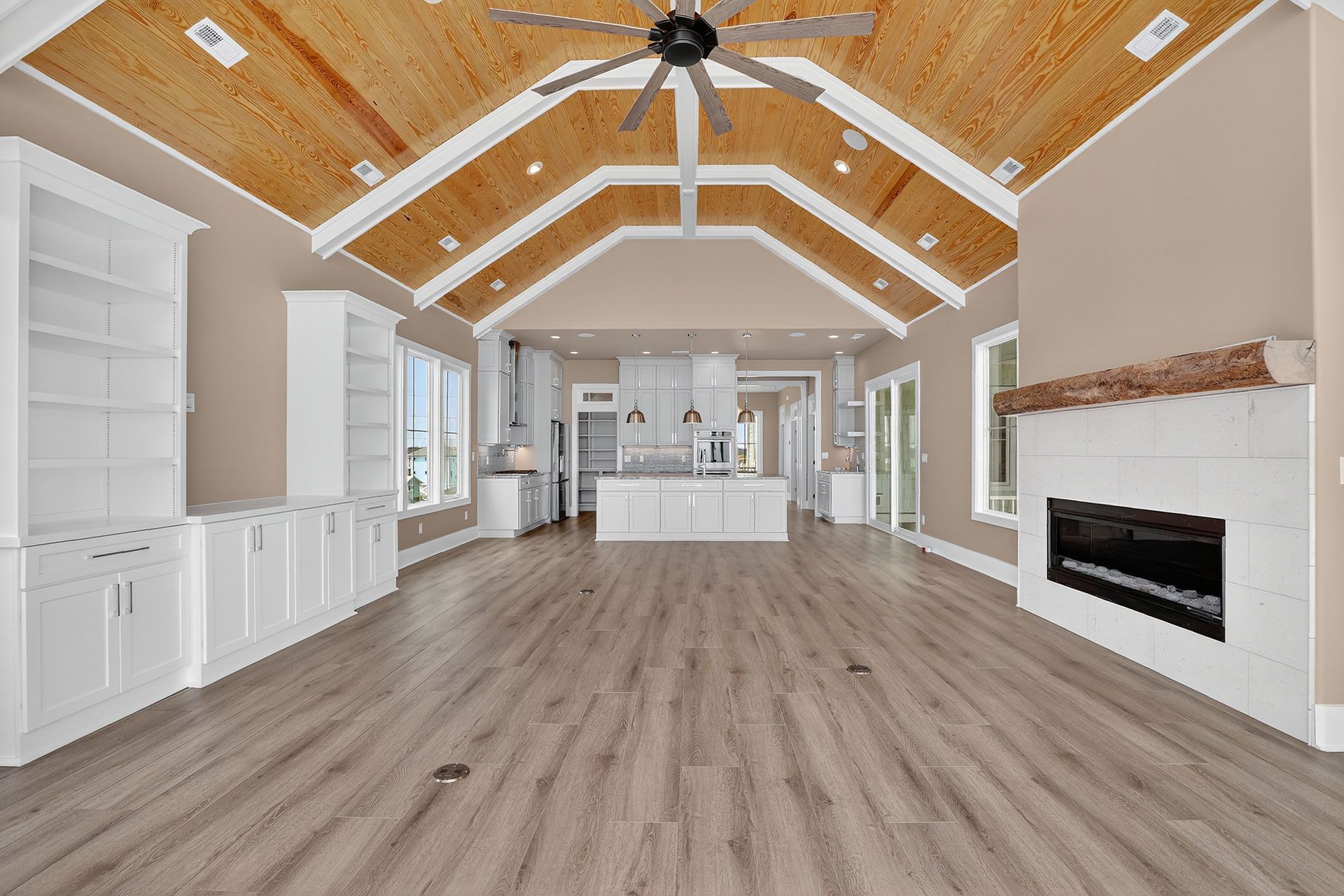 Open-concept living space with light wood floors, vaulted wood ceiling, white cabinets, and fireplace.