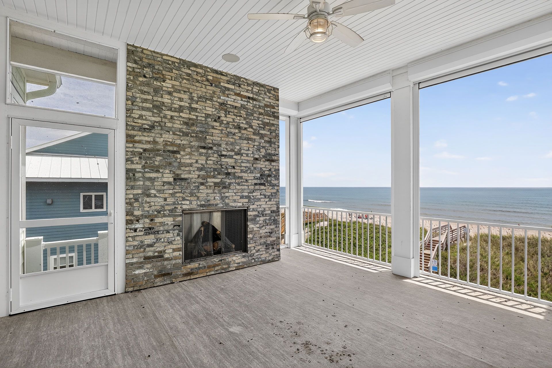 Screened porch with stone fireplace, ocean view, white columns, blue sky.
