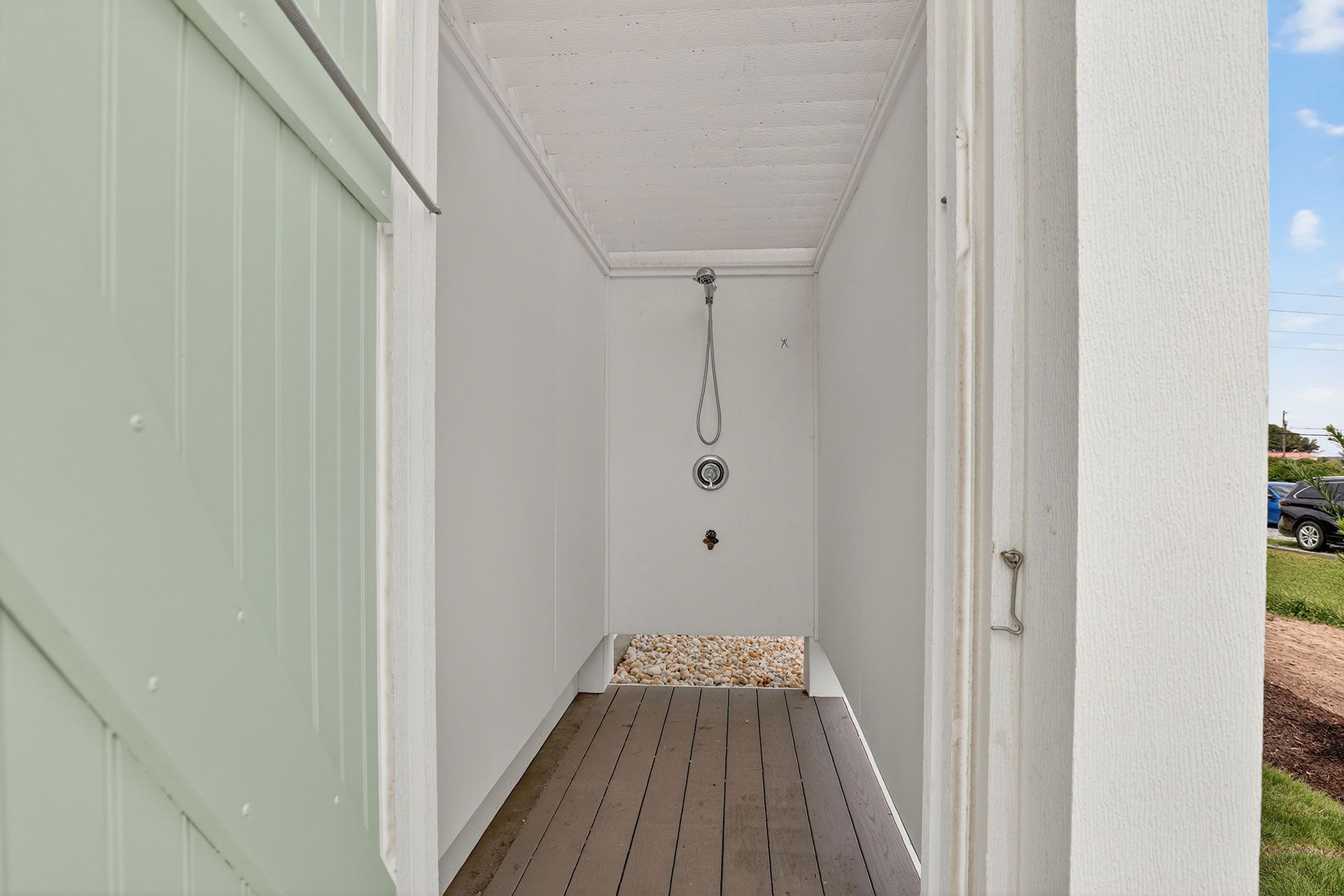 Outdoor shower stall with wooden floor, white walls, and a green door.