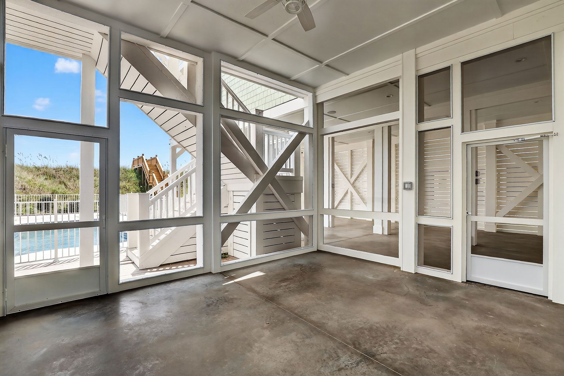 Sunroom with white trim, screened windows, and concrete floor; stairs lead outside to a blue sky.