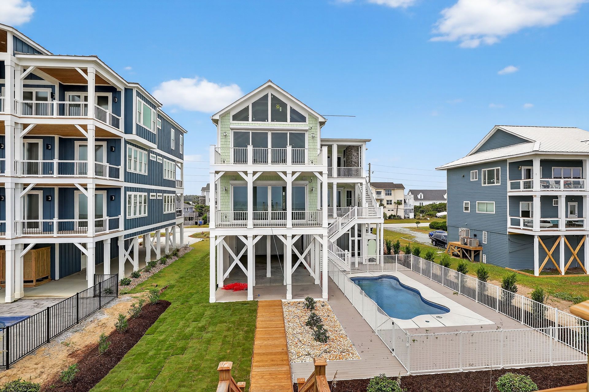 Three-story beach houses with white framing, green siding, and a pool under a blue sky.