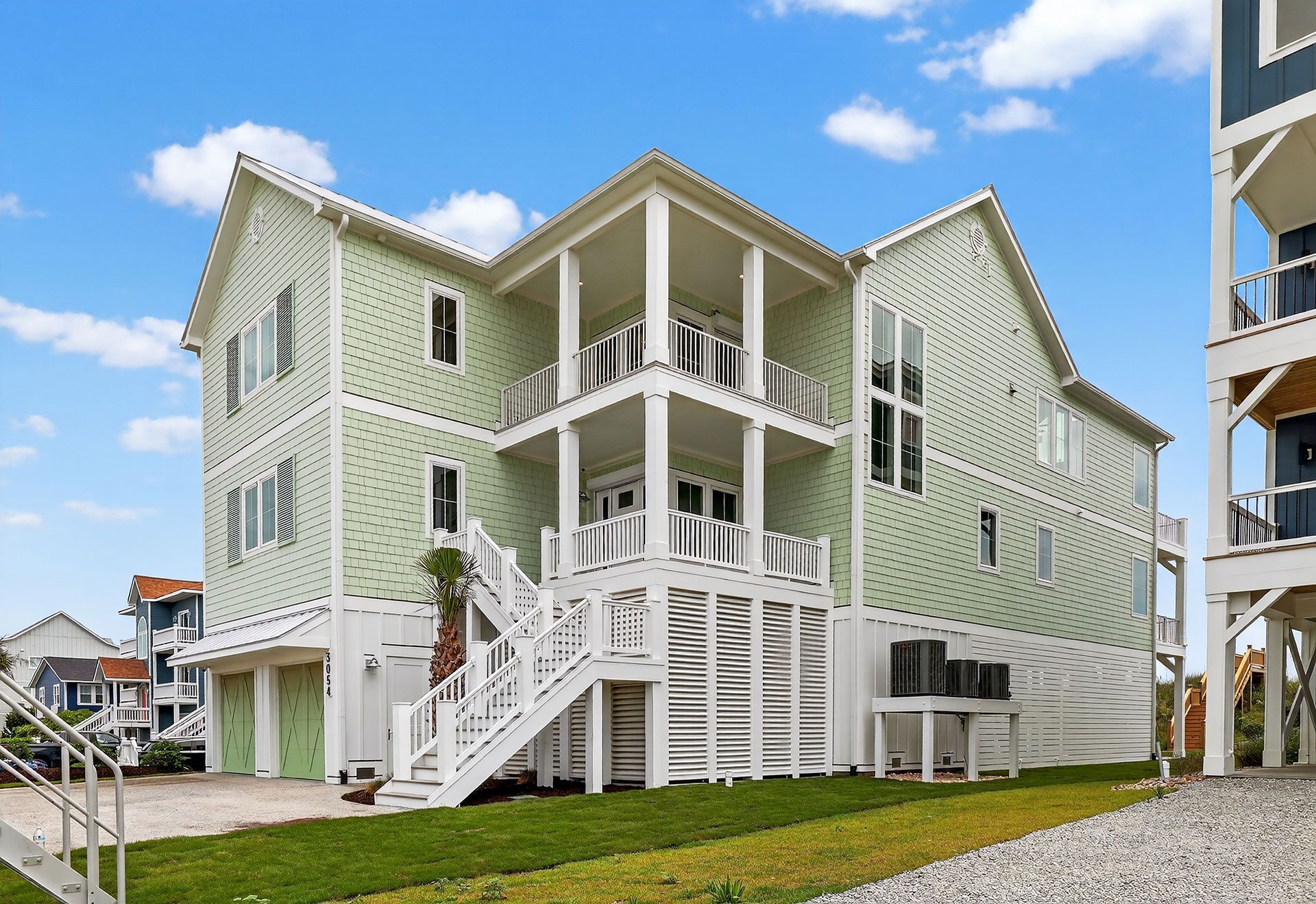 Beach house with light green siding, white trim, balconies, and stairs. Blue sky in the background.