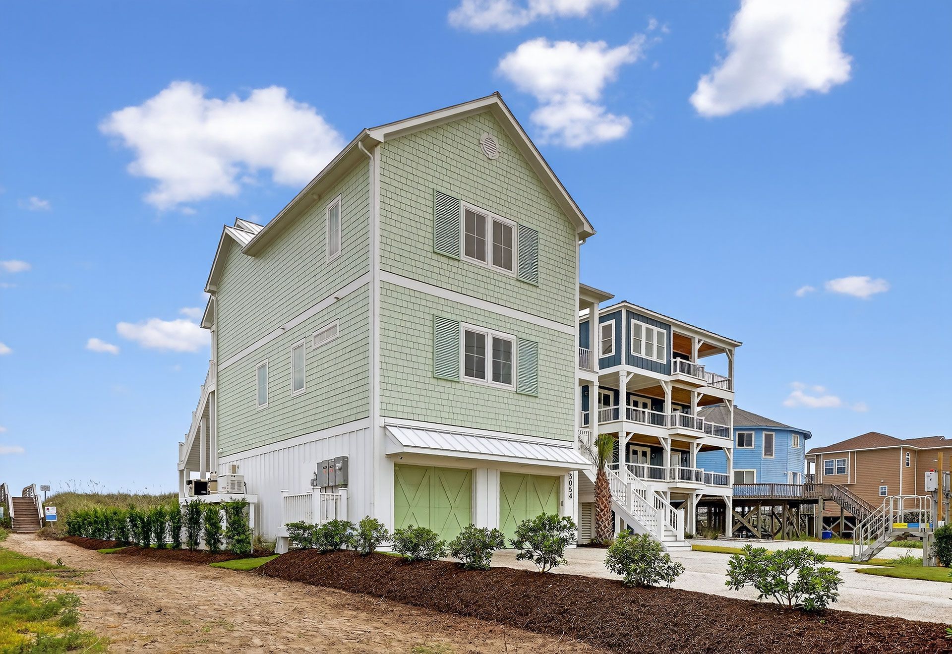 Green beach house with white trim against a blue sky.