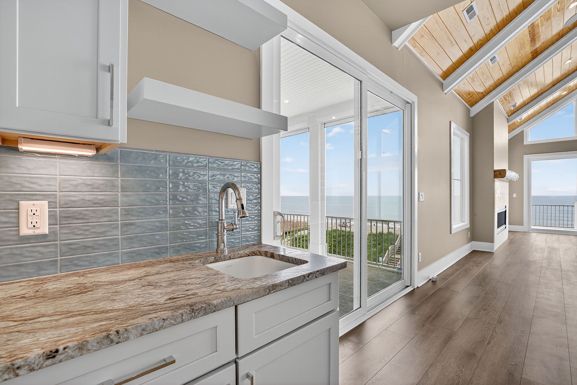 Kitchen with sink, cabinets, granite countertop, and ocean view through sliding glass doors.