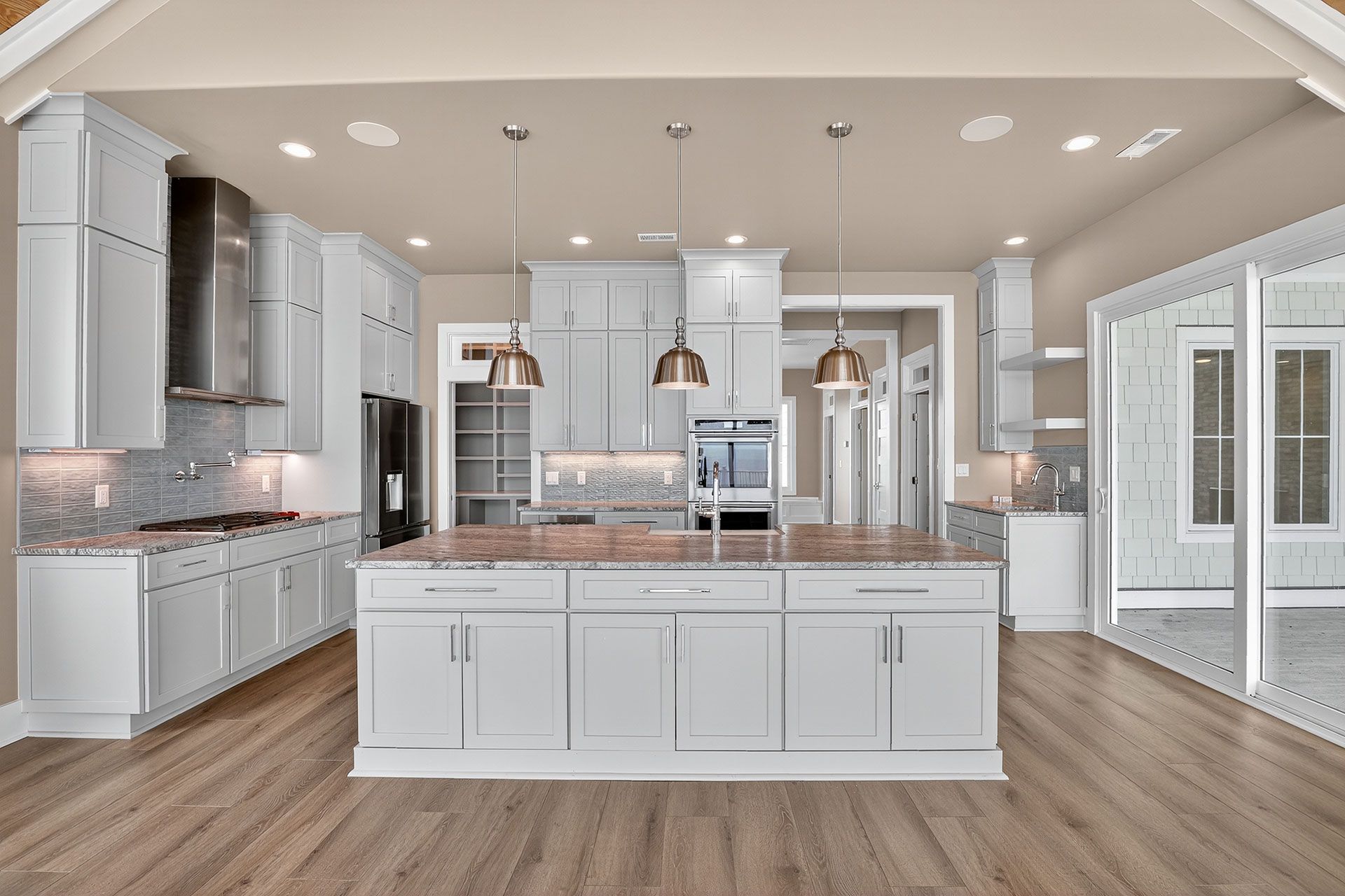 Modern light-grey kitchen with a large island, stainless steel appliances, and light wood floors.