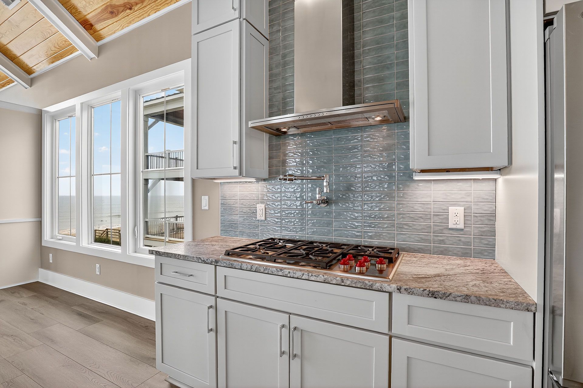Modern kitchen with white cabinets, granite counters, gas stove, and blue tile backsplash.