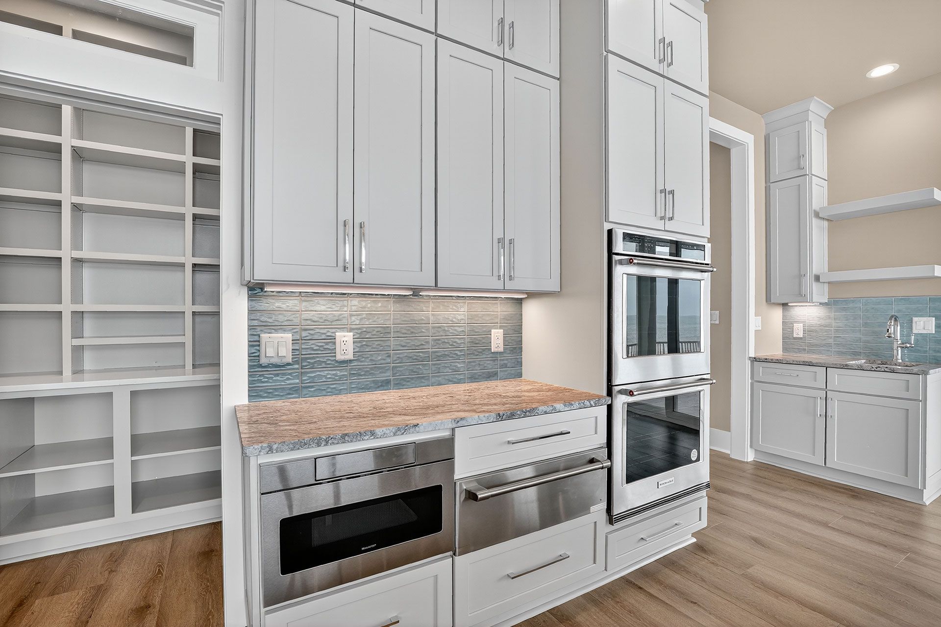 Light gray kitchen with pantry, granite counters, stainless steel appliances, and blue backsplash.