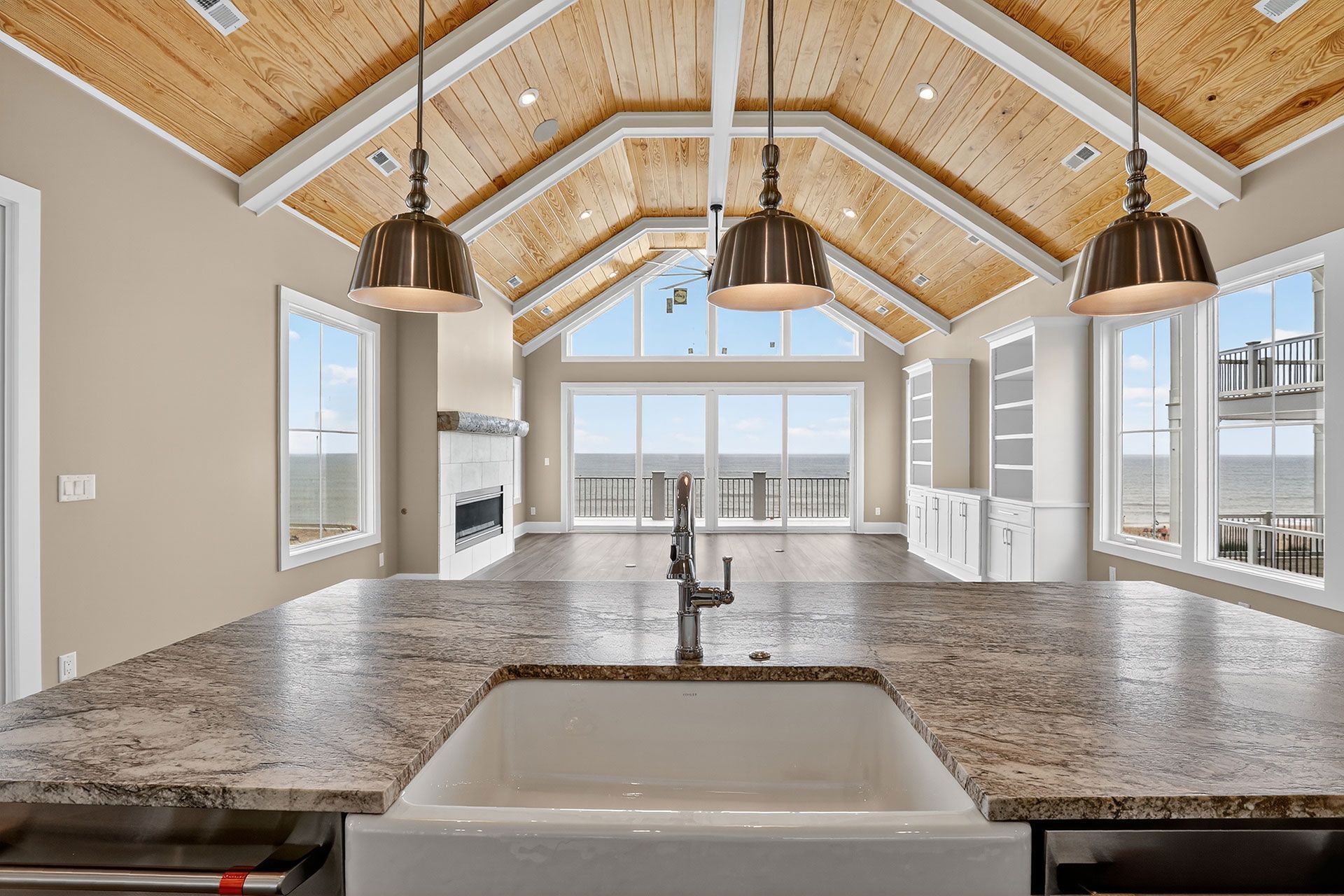 Kitchen with a farmhouse sink, granite countertops, and a vaulted, wood-paneled ceiling; a fireplace and ocean view.