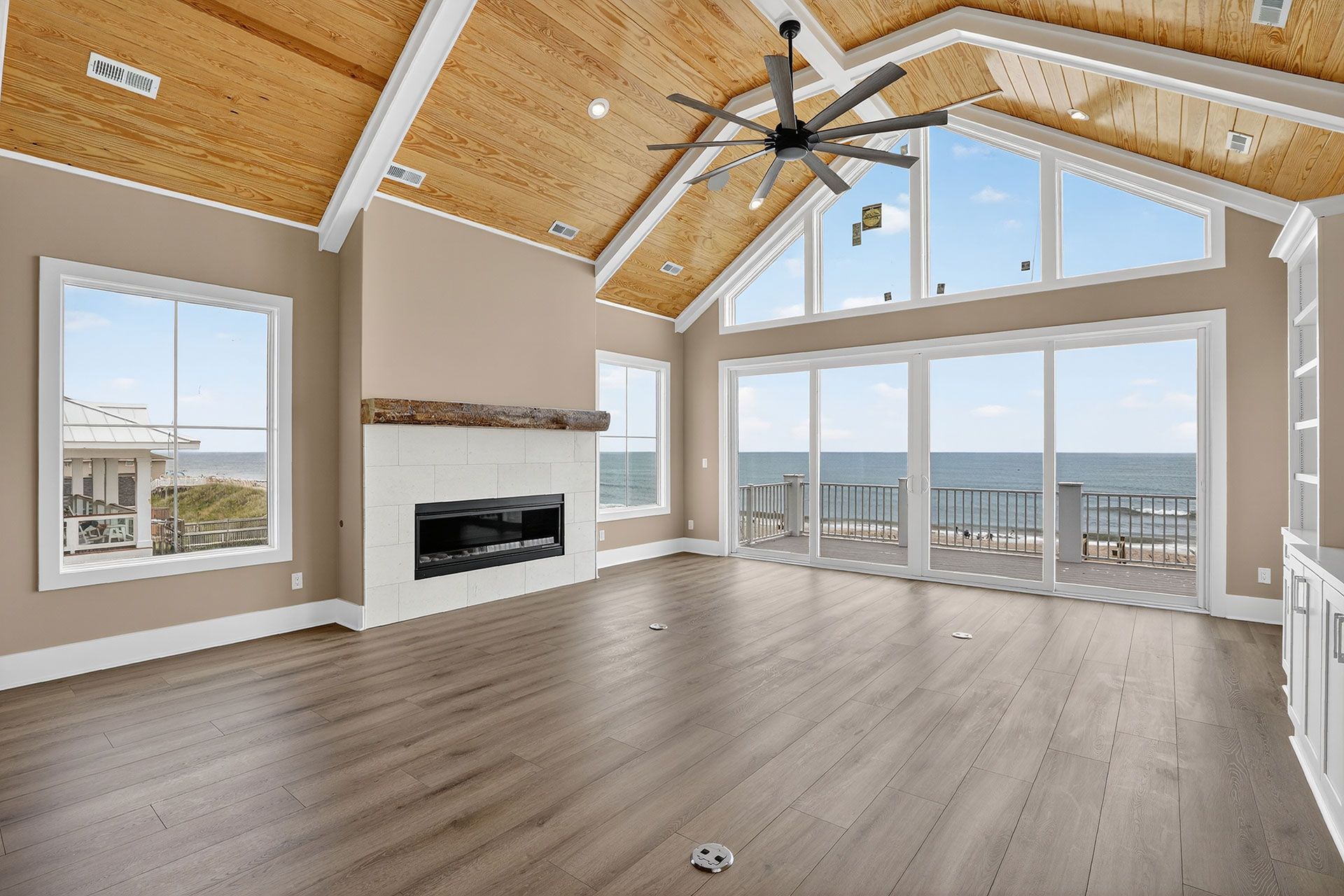 Spacious living room with ocean view, vaulted wood ceiling, fireplace, large windows, and wood floors.