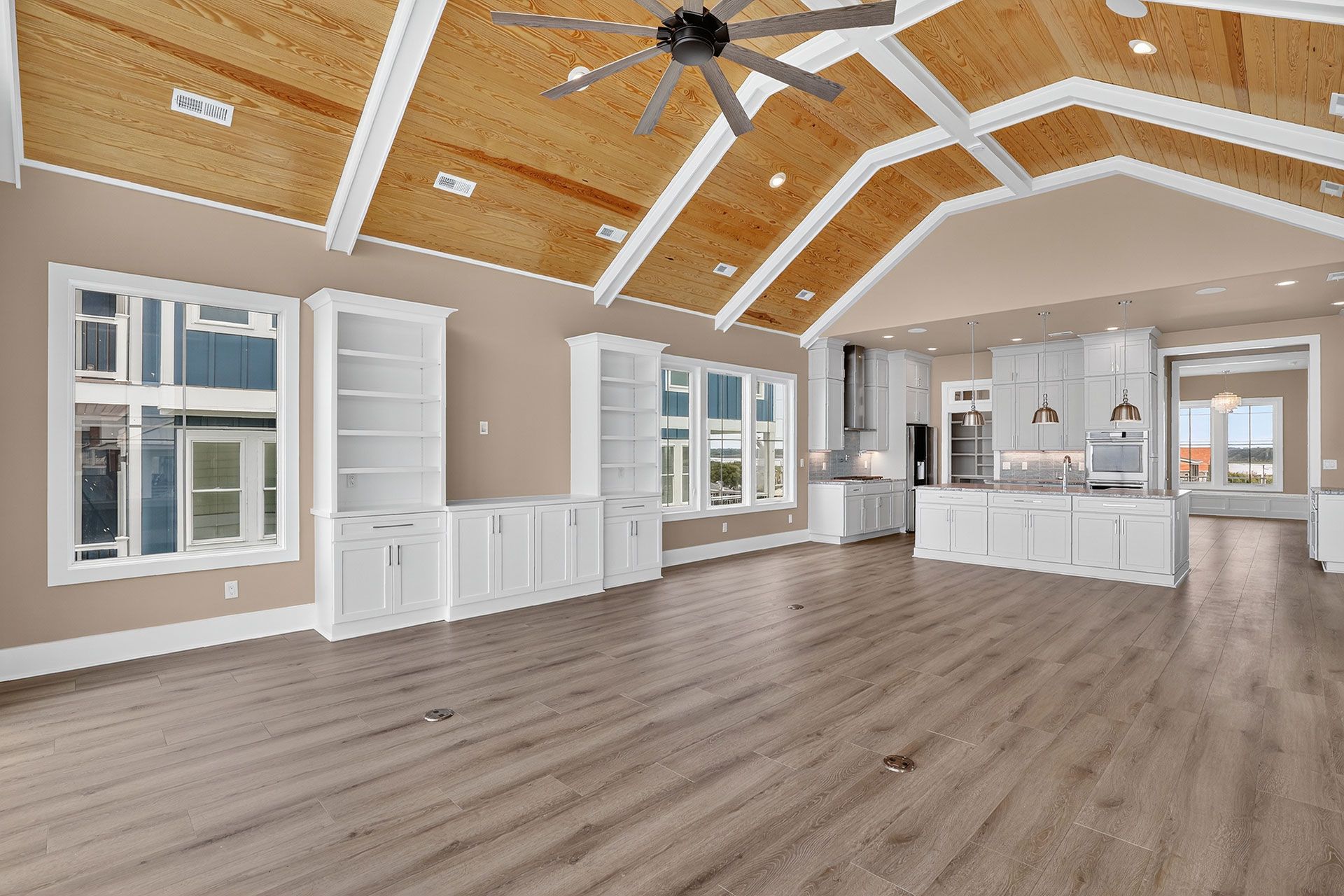 Spacious living area with vaulted wood ceiling, white cabinetry, and light wood flooring.