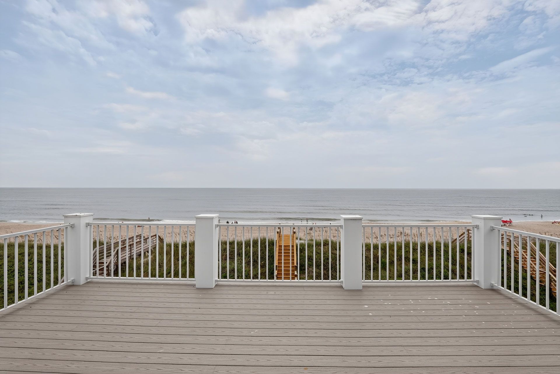 Ocean view from a deck with white railing. Beach and sky in the background.
