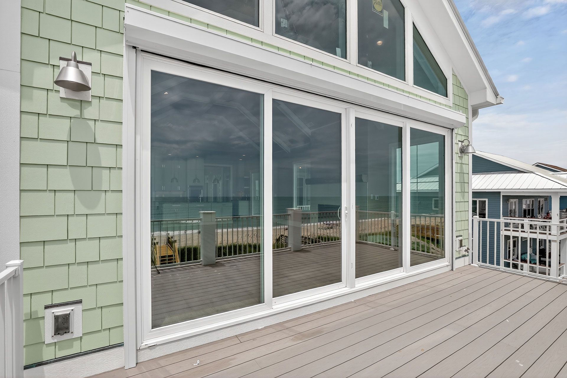 Large glass sliding doors on a beach house deck, overlooking the water.