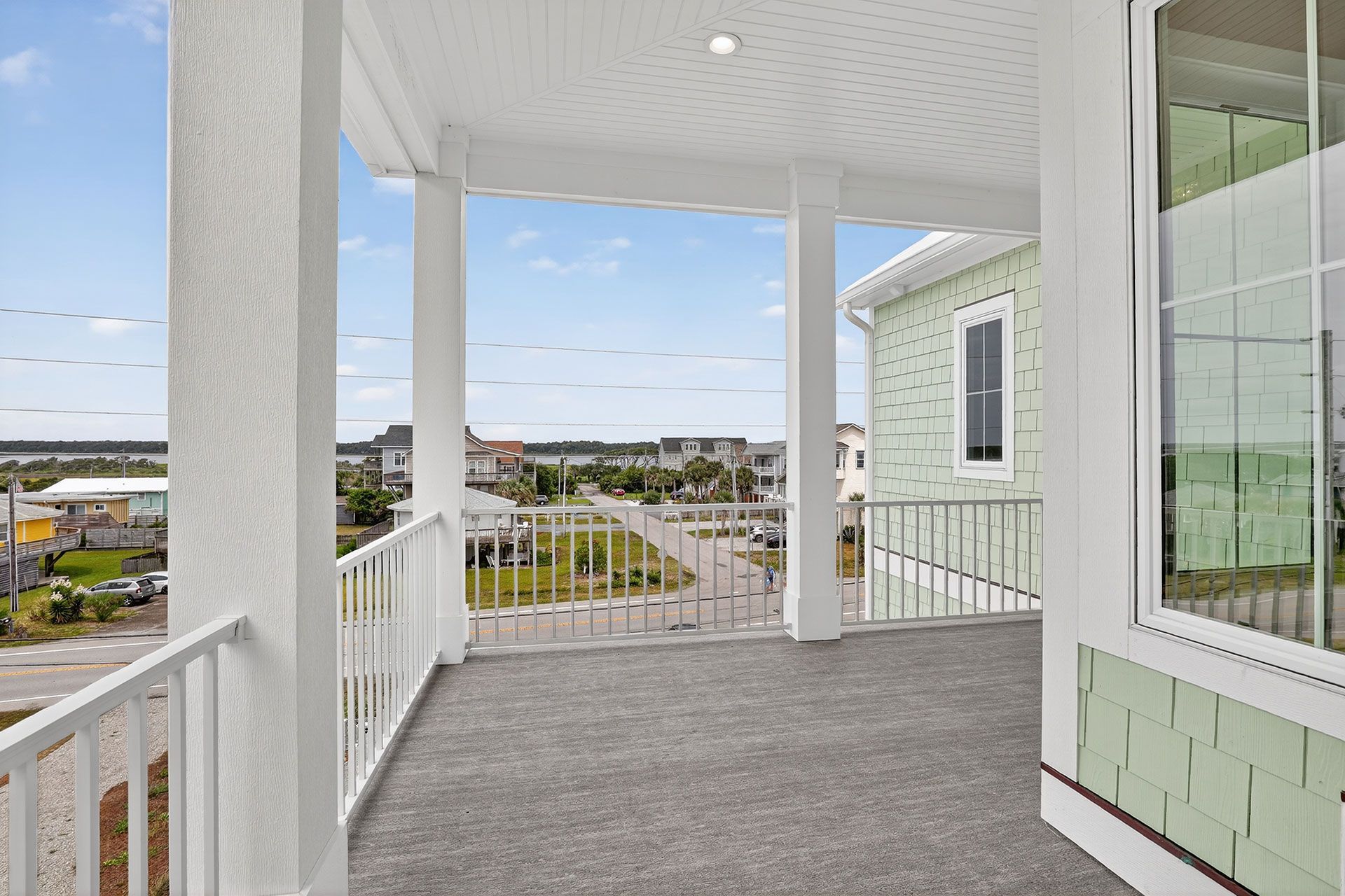 Balcony overlooking a coastal town, white railings, columns, and light green siding.