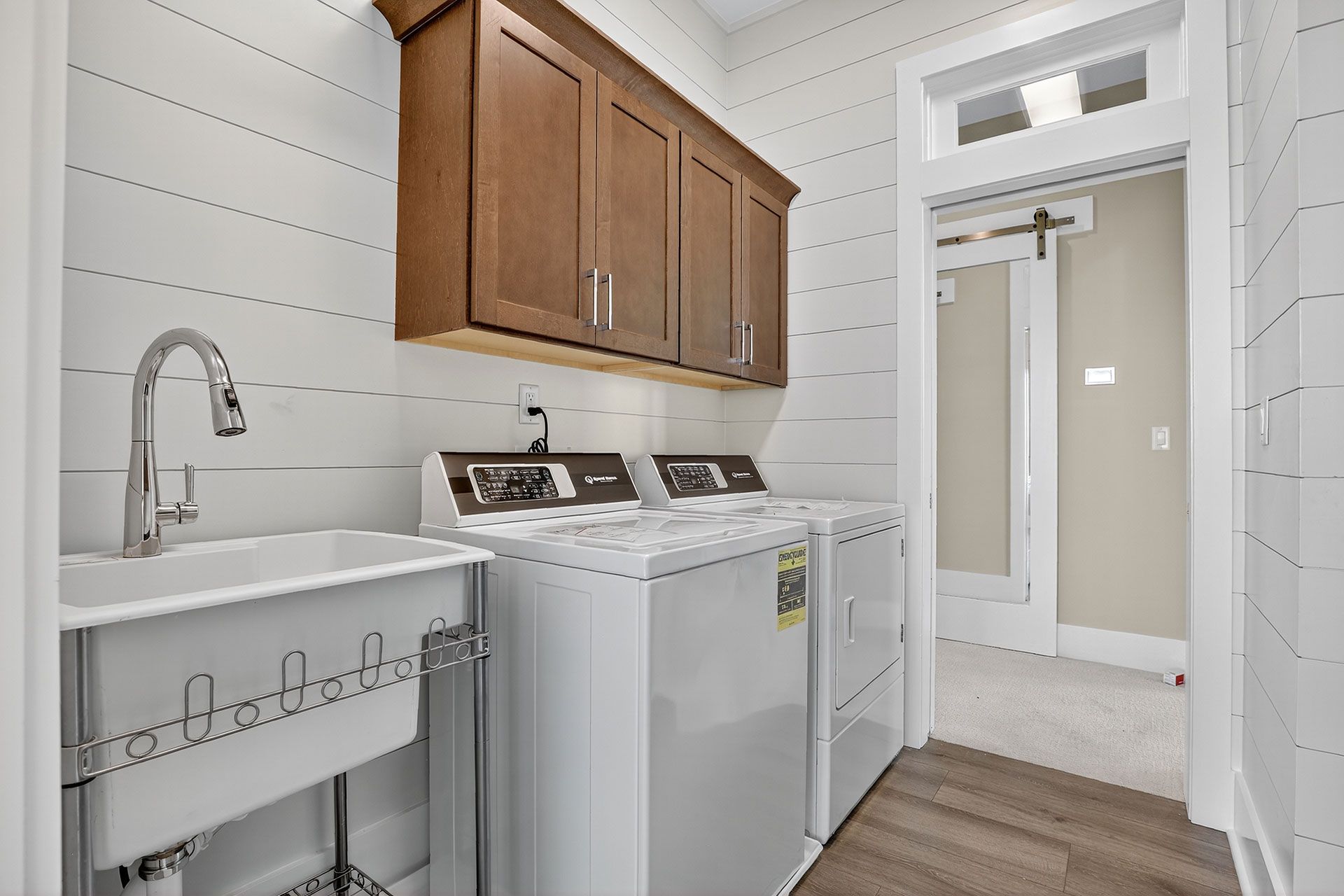 Laundry room with white appliances, brown cabinets, and a utility sink.