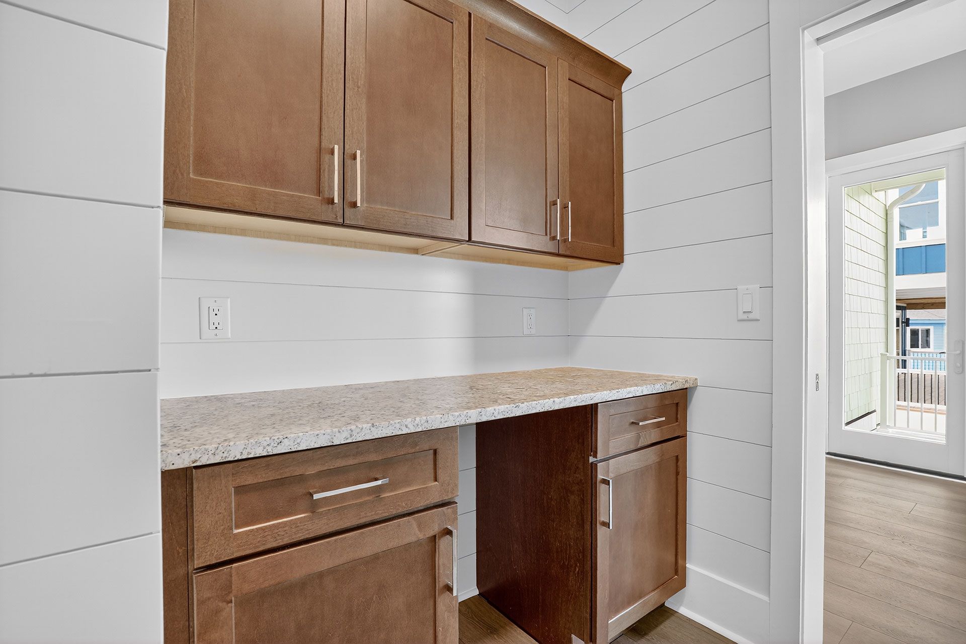 Built-in desk with upper cabinets in a room with white shiplap walls and an open doorway.
