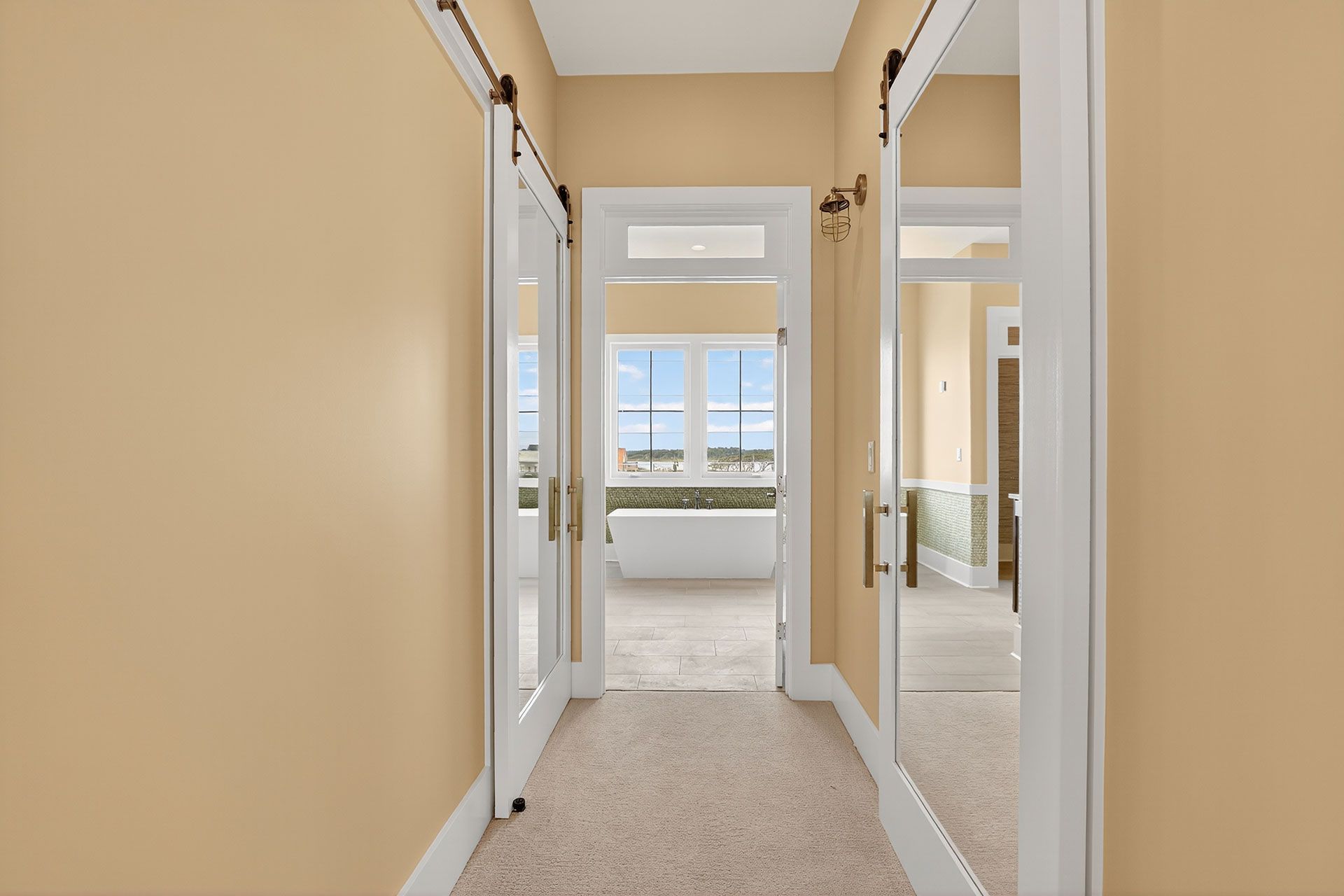 Hallway with beige walls, carpet, and mirrored doors leading to a window with an outdoor view.