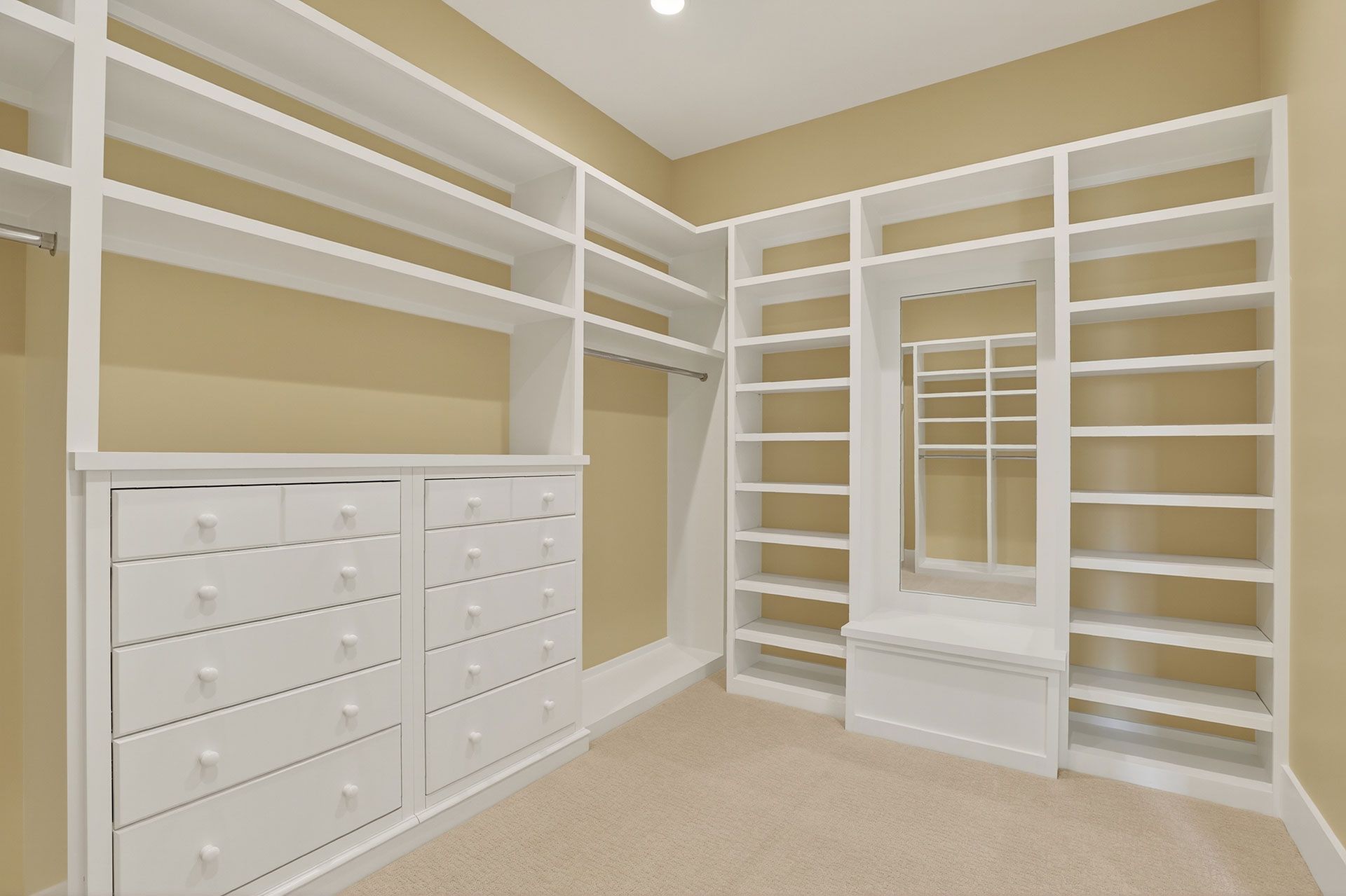 White walk-in closet with built-in shelves, drawers, and hanging rods. Cream walls and beige carpet.