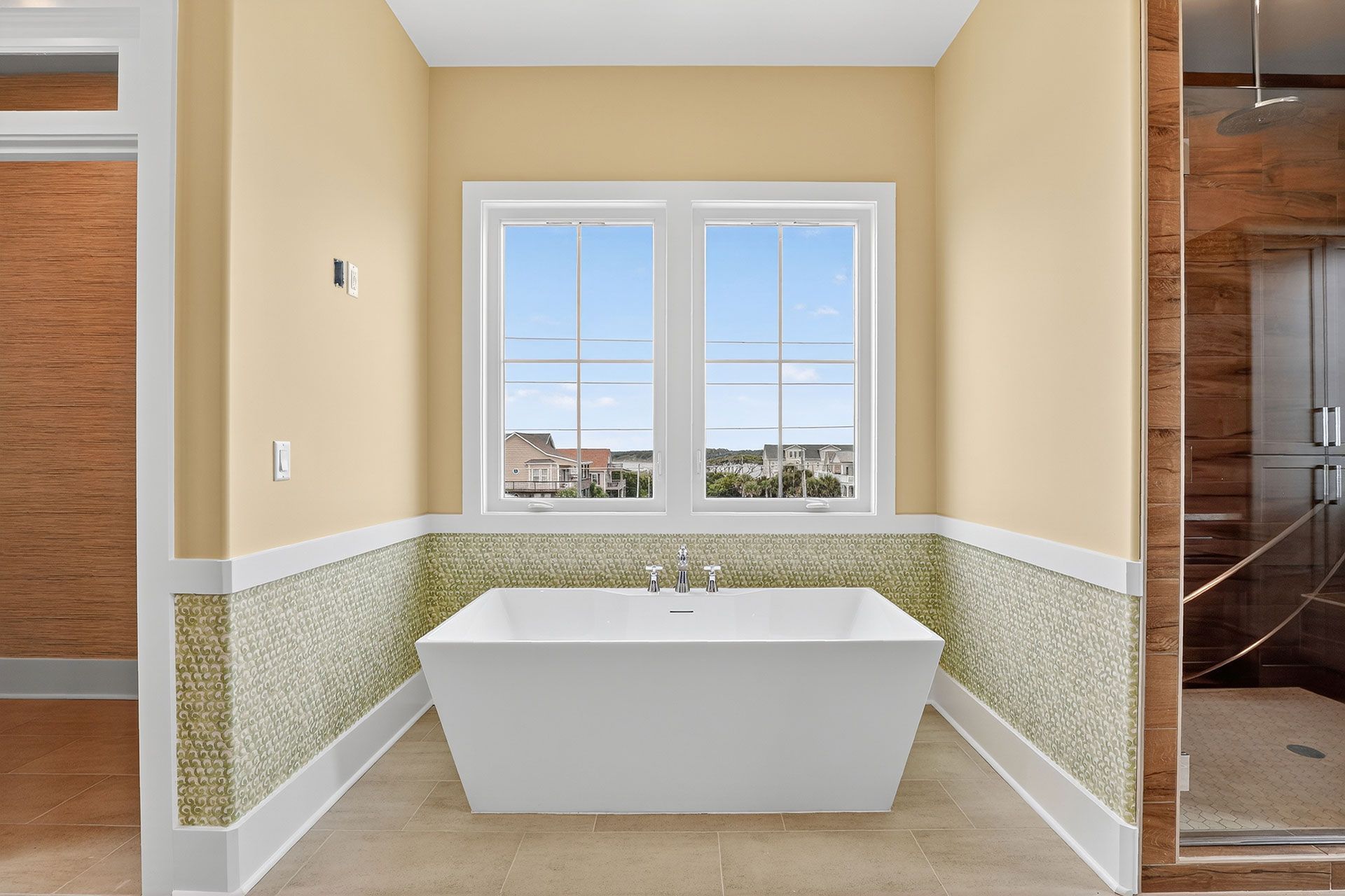 Spacious bathroom with white freestanding tub under a window. Walls are light yellow with mosaic tile accents.