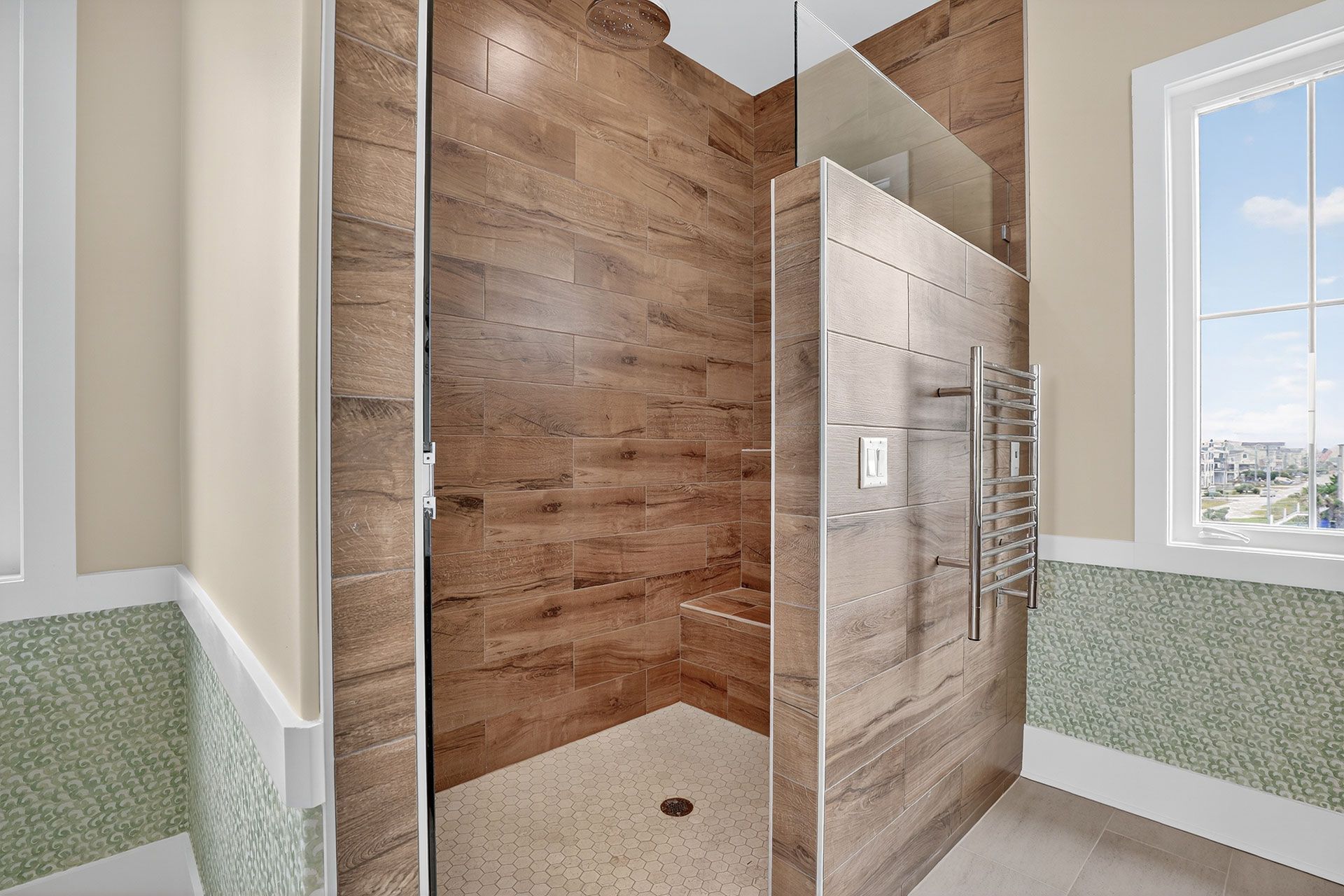 Bathroom with walk-in shower featuring brown tile, glass, and a heated towel rack; window with white trim.