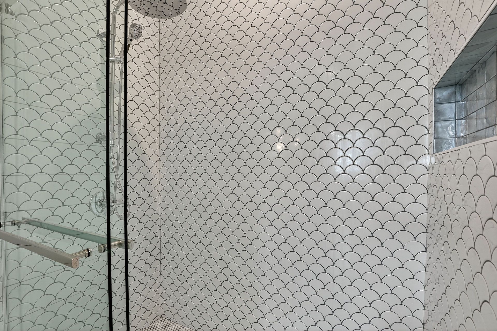 Shower with fish-scale patterned white tiles and glass door; a small window is on the right.