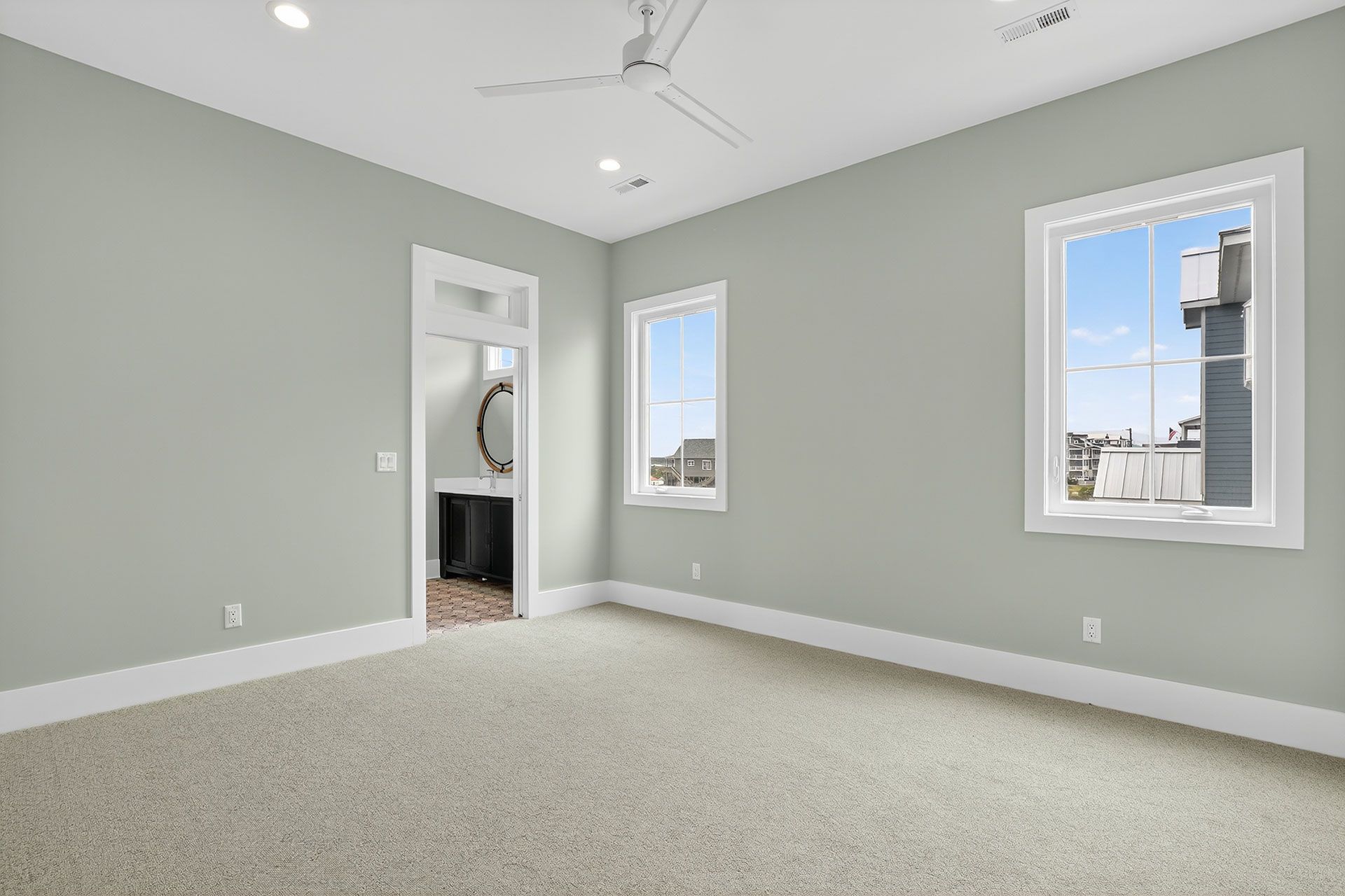 Empty bedroom with light green walls, two windows, carpet, and a doorway to a small bathroom.