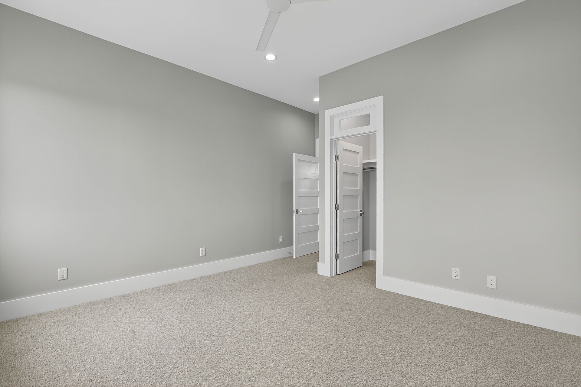 Empty bedroom with gray walls, white trim, carpet, and two doorways.