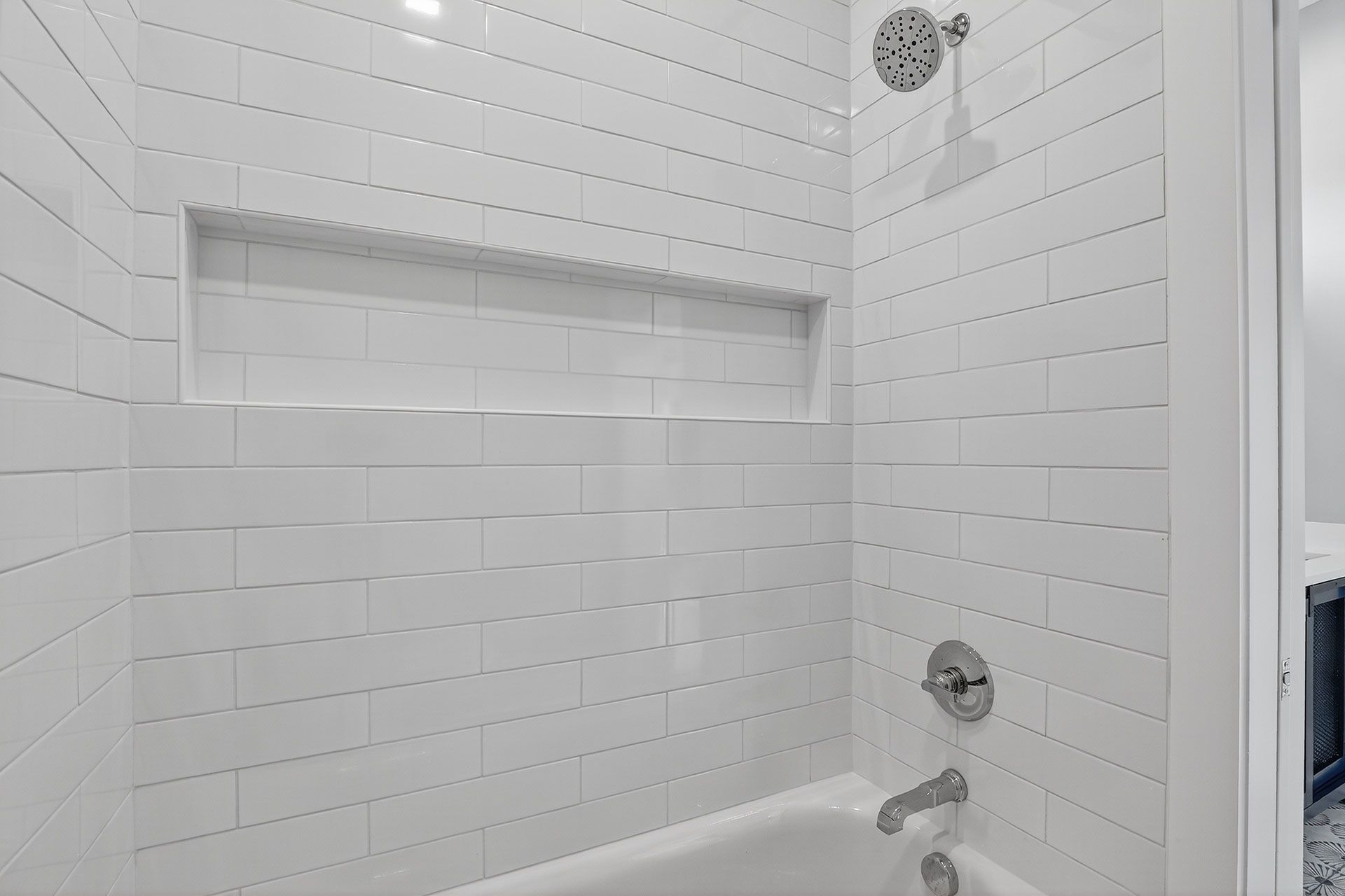 White tiled shower with built-in shelf and silver fixtures.