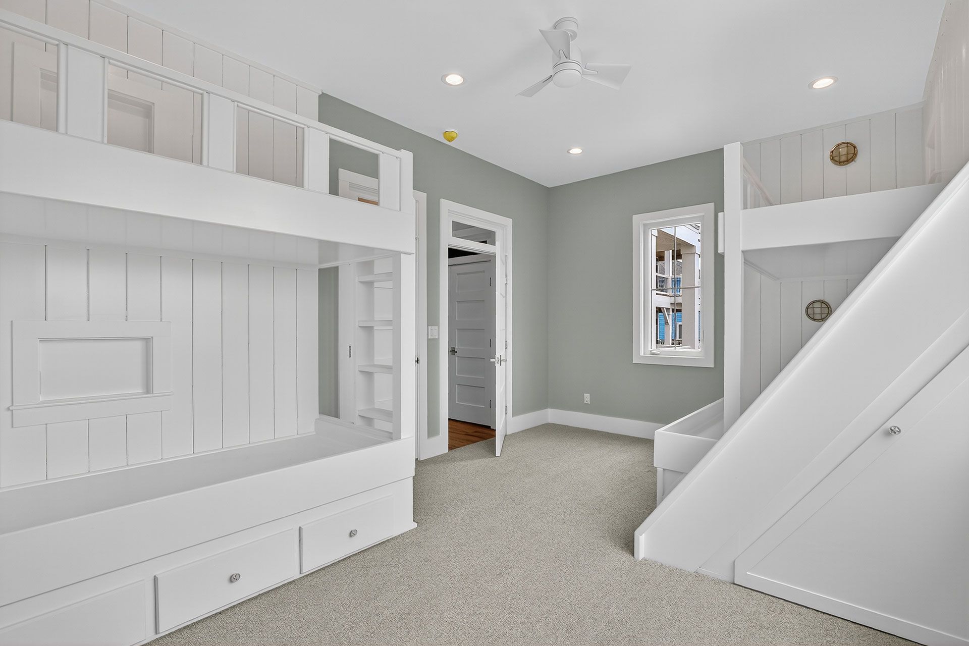 White bunk beds with slide in a bedroom with neutral carpet and blue-gray walls.