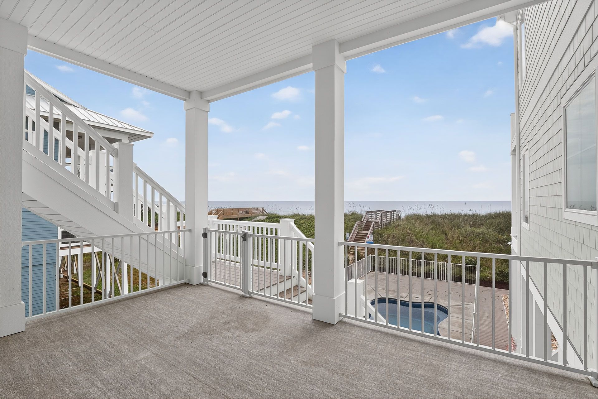 Balcony overlooking ocean and trees with white railings and columns. Bright sunny day.