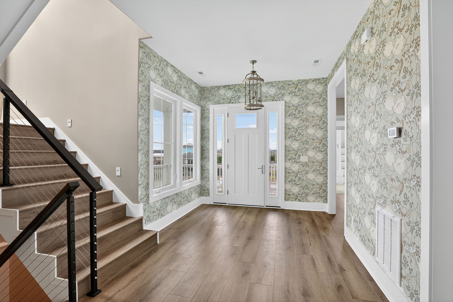 Entryway with stairs on the left, patterned wallpaper, and a door with sidelights.