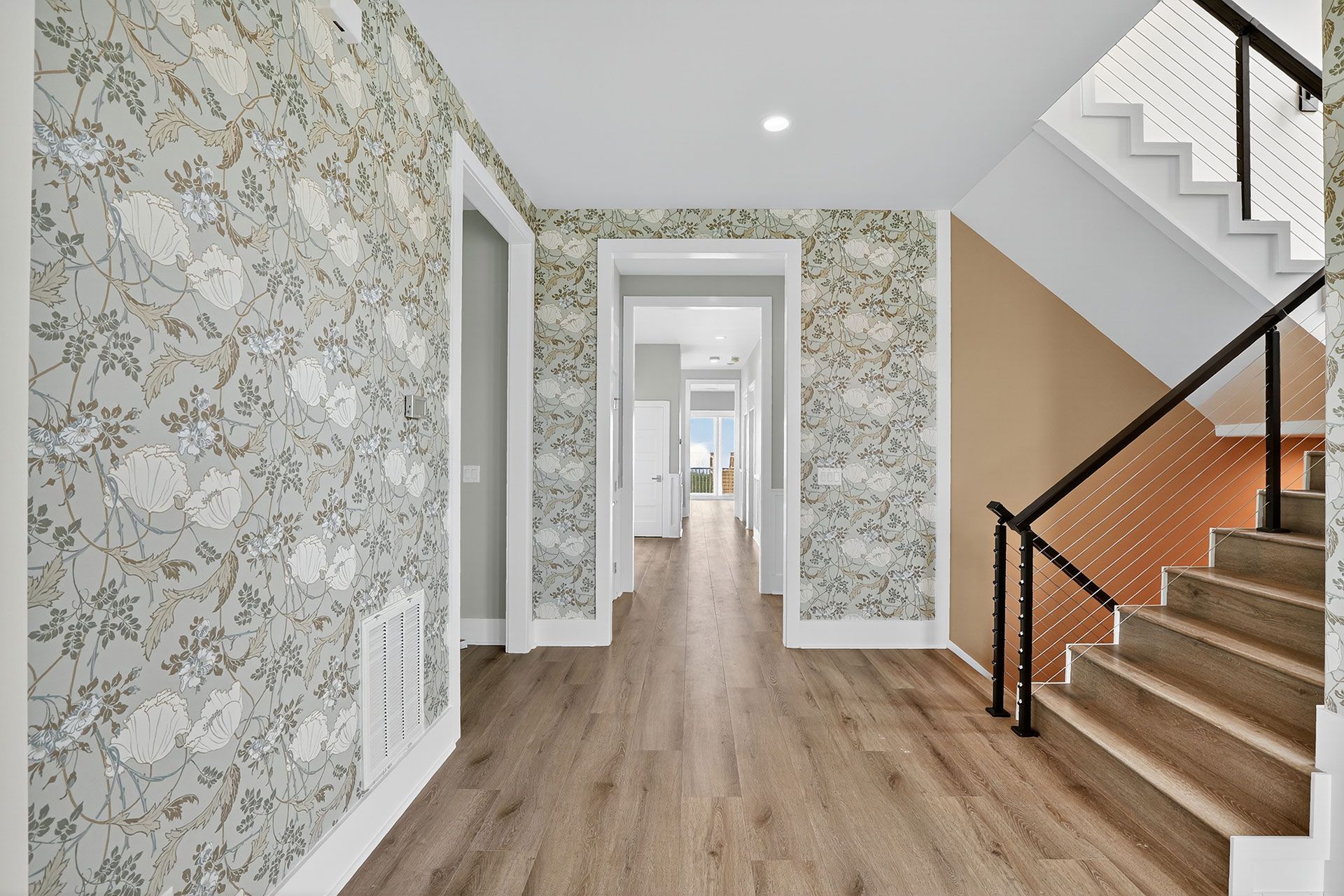 Hallway with floral wallpaper, wooden floors, and staircase with black railing.