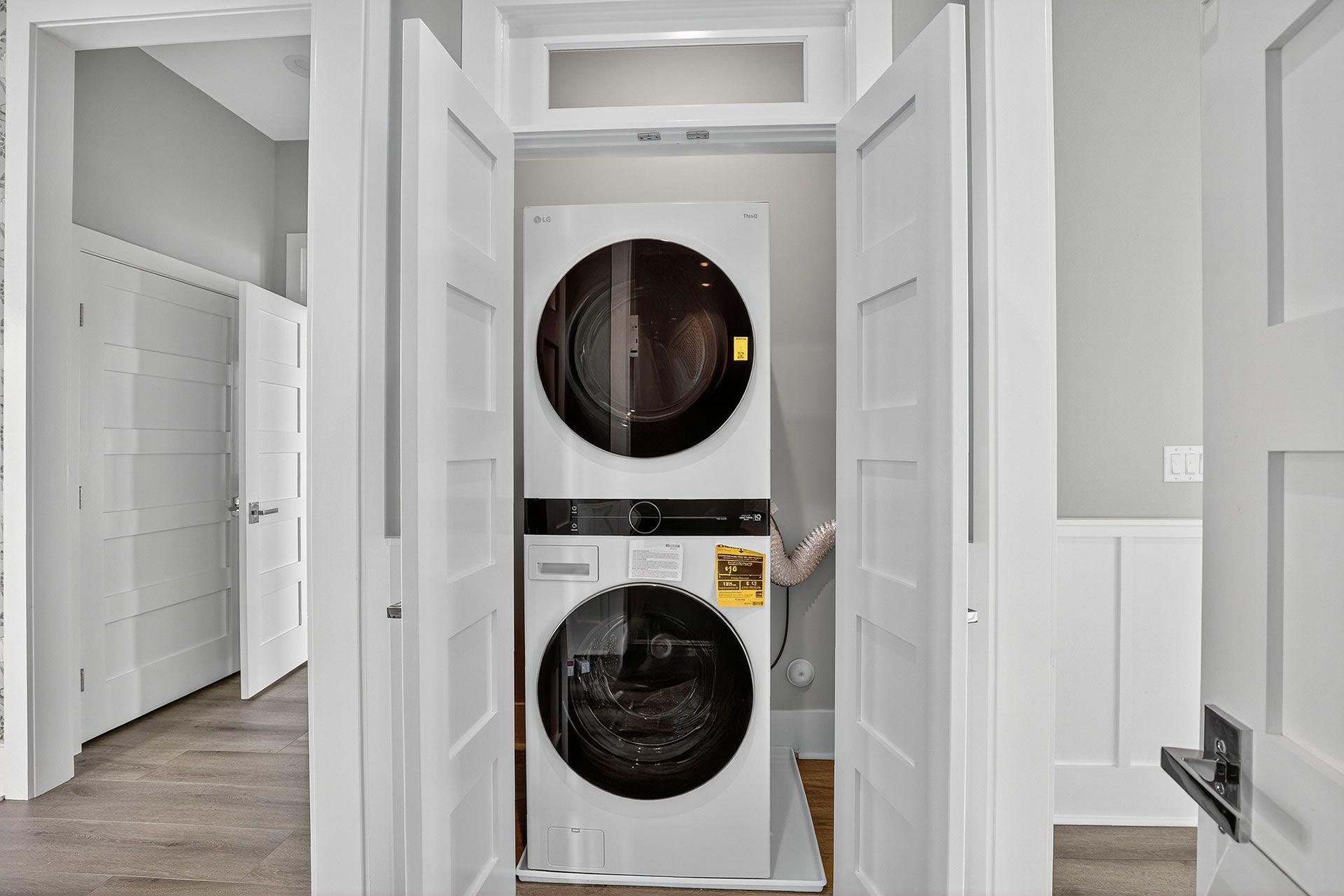 Stacked white washer and dryer unit in a closet with open white doors.