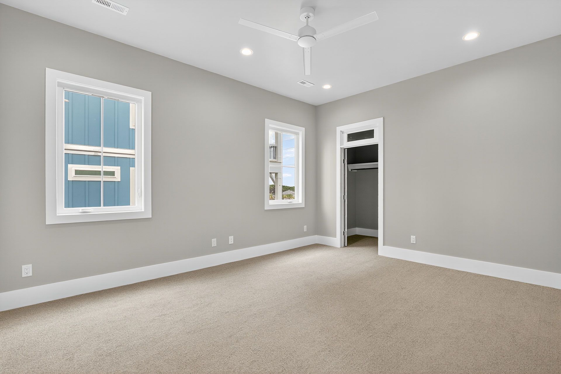 Empty bedroom with gray walls, white trim, tan carpet, and two windows.