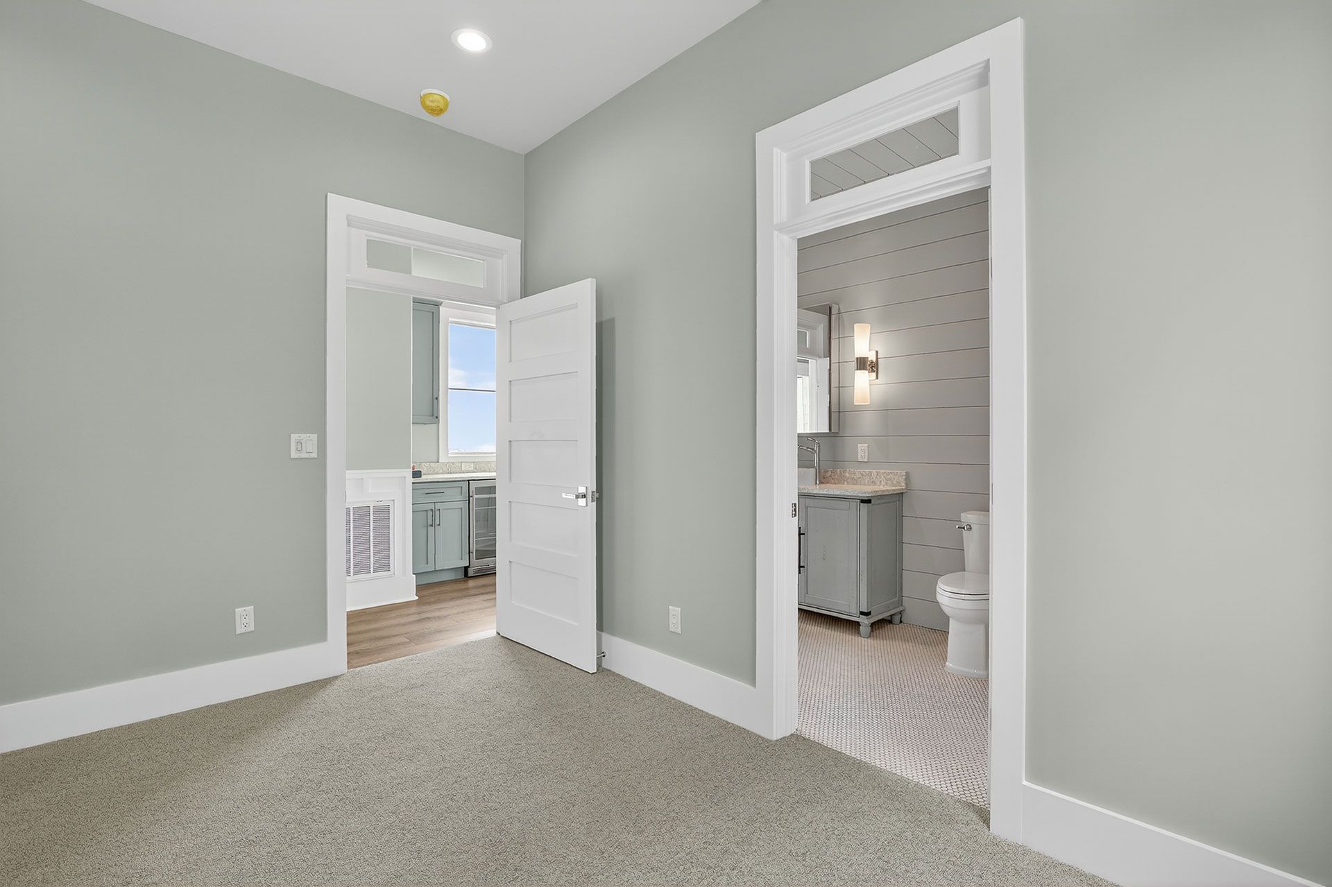 Bedroom with an open doorway to a bathroom; gray walls, white trim, carpet, blue vanity.