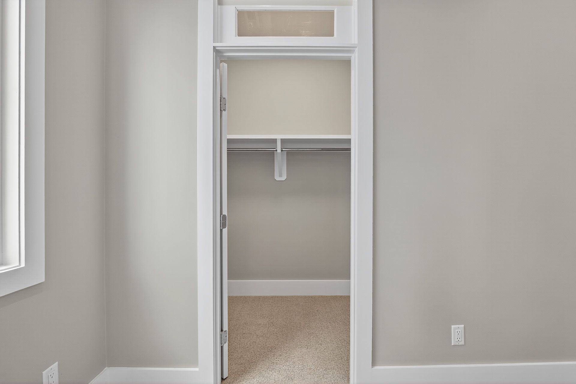 Empty closet with beige carpet and a shelf, framed by white trim, in a room with gray walls.