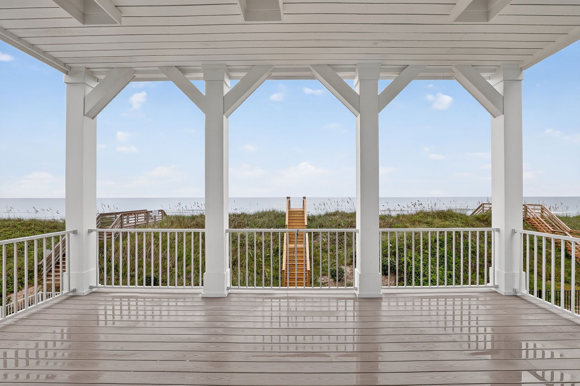 White porch overlooking the ocean. A wooden staircase leads to the beach.