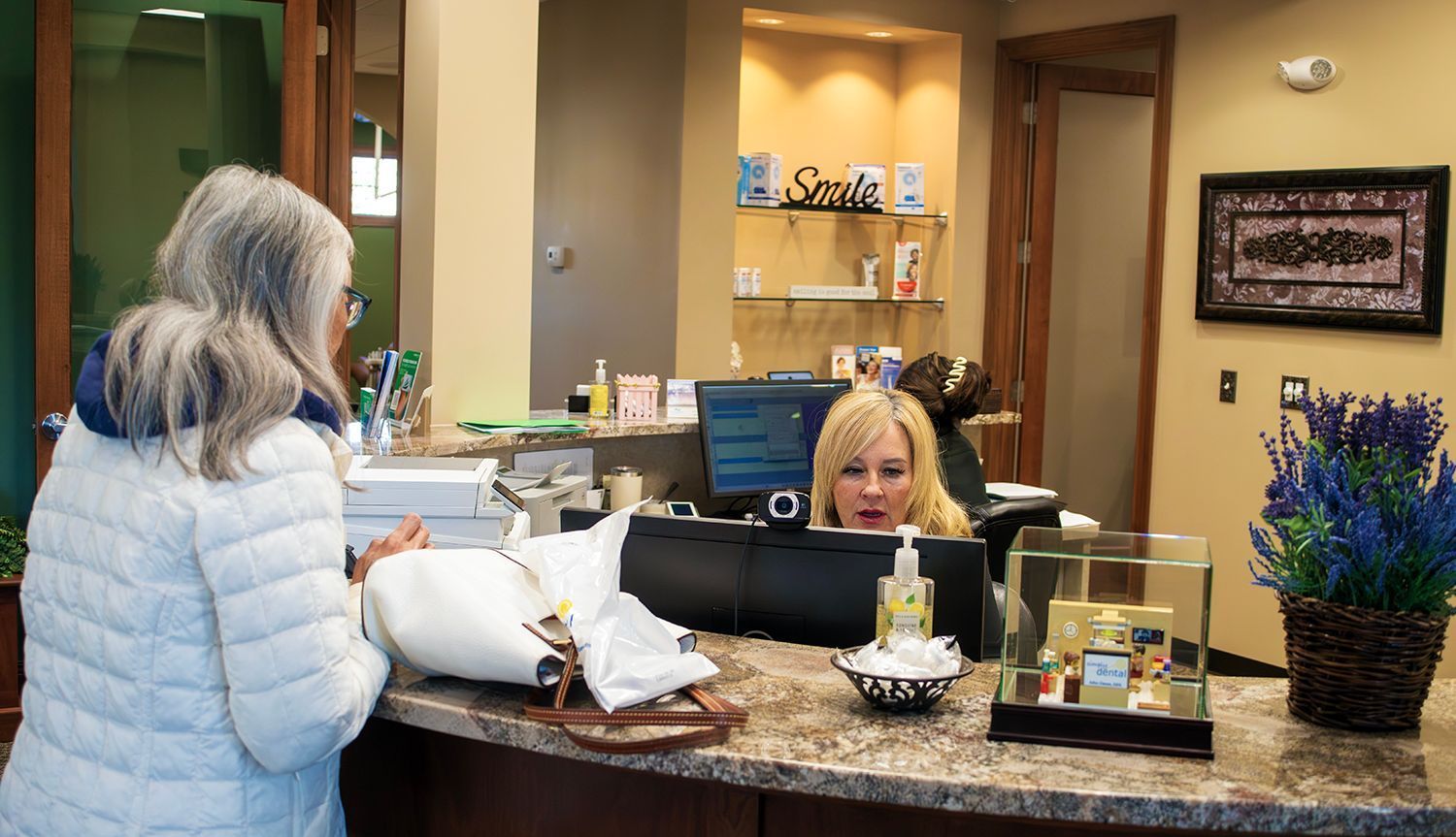 A patient at a medical office reception desk interacts with a staff member behind a counter.