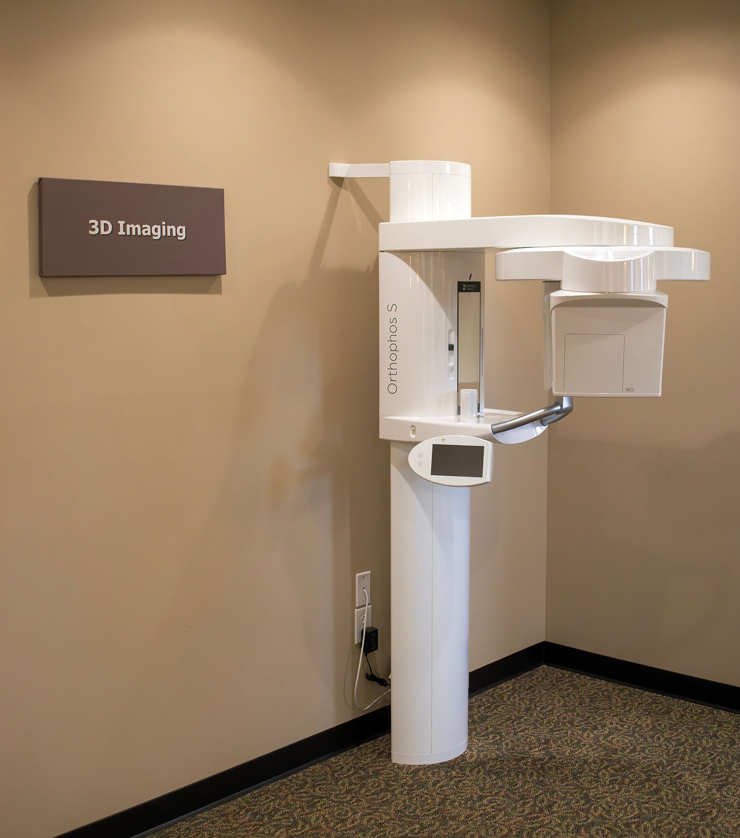 A white 3D dental imaging machine mounted to a beige wall in an office with a sign labeled 3D Imaging.