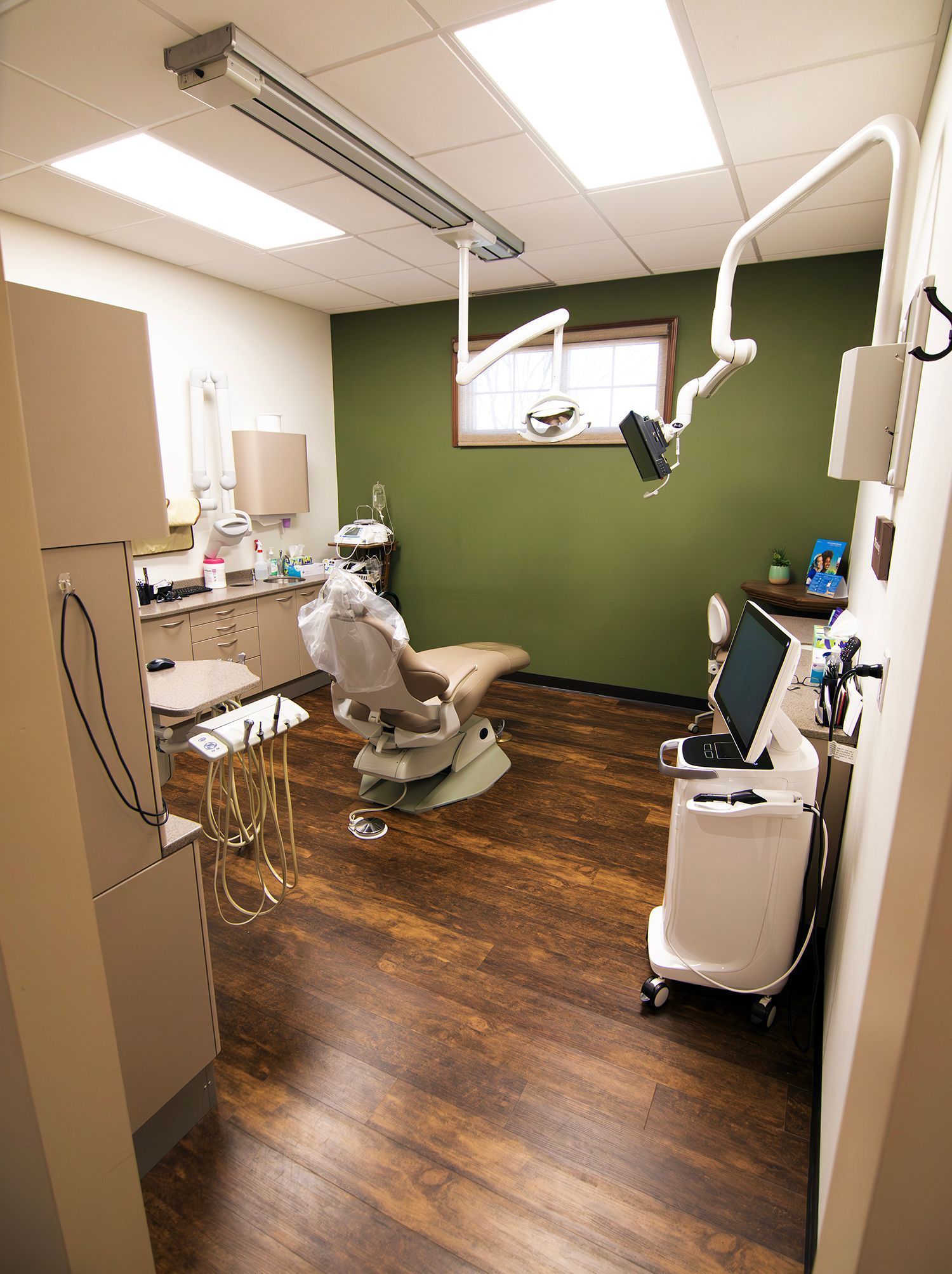 A well-lit dental exam room with a reclining chair, equipment, and a green accent wall.
