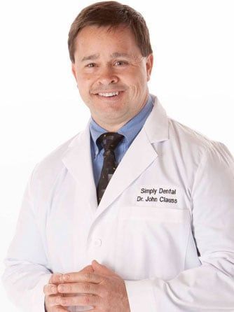 Man in white lab coat smiles; Simply Dental sign says