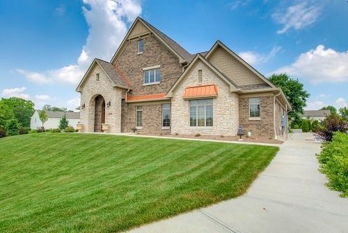 Brick and stone two-story house with green lawn and a clear, blue sky.