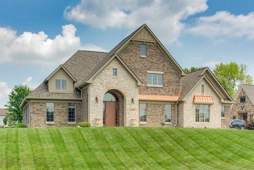 Two-story house with brick and stone exterior, copper accents, and a sloped green lawn under a partly cloudy sky.