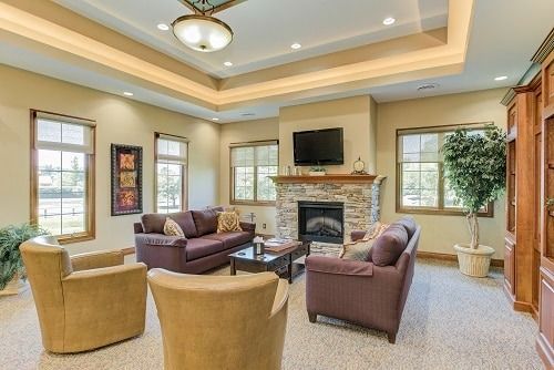 Living room with couches, fireplace, TV, and windows. Beige walls, neutral-toned furniture.