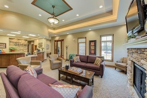 Spacious waiting area with couches, fireplace, and reception desk. Light-colored walls and carpet.